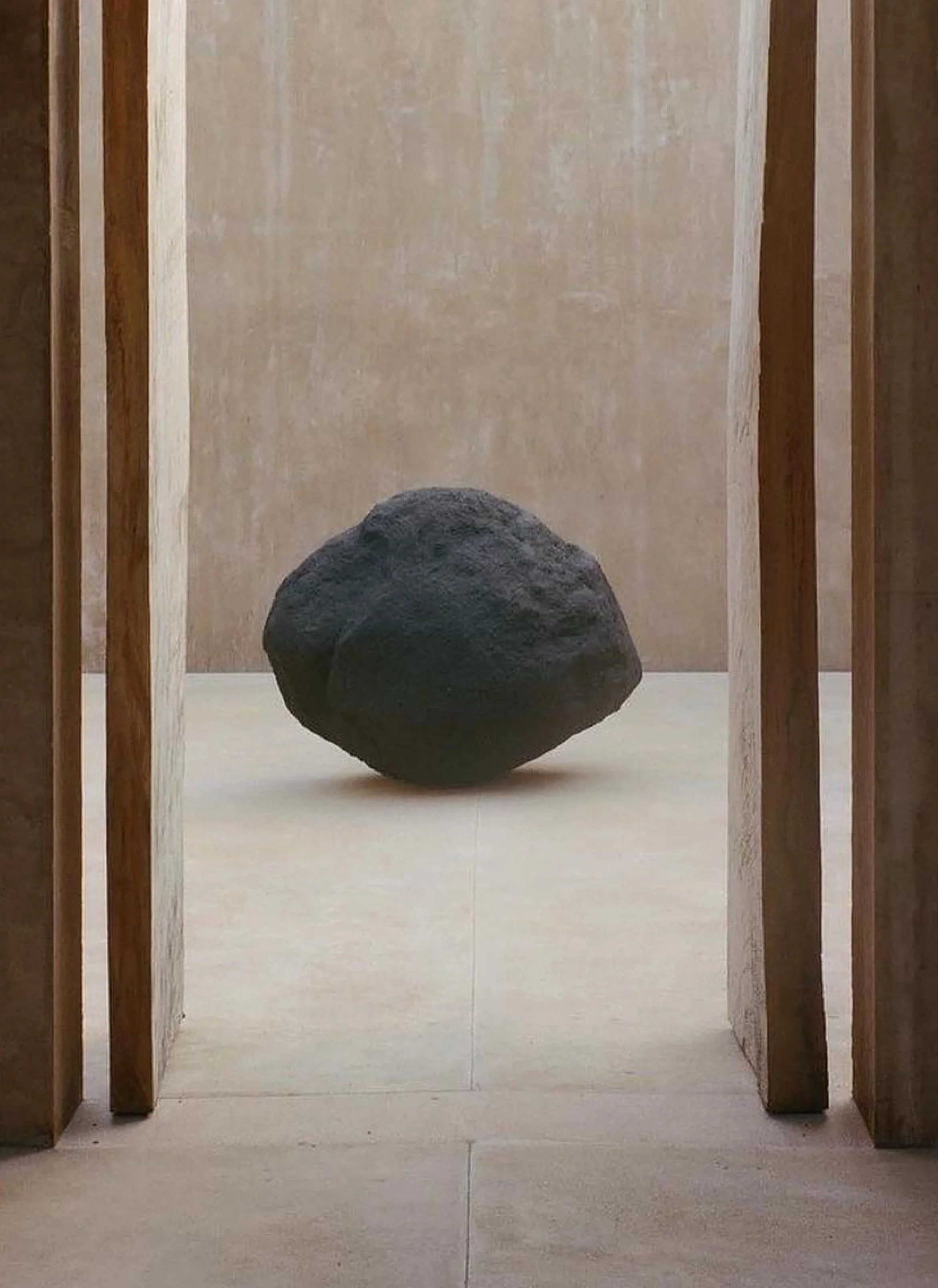 A black rock on a beige floor, framed by wooden panels, with a beige wall in the background.