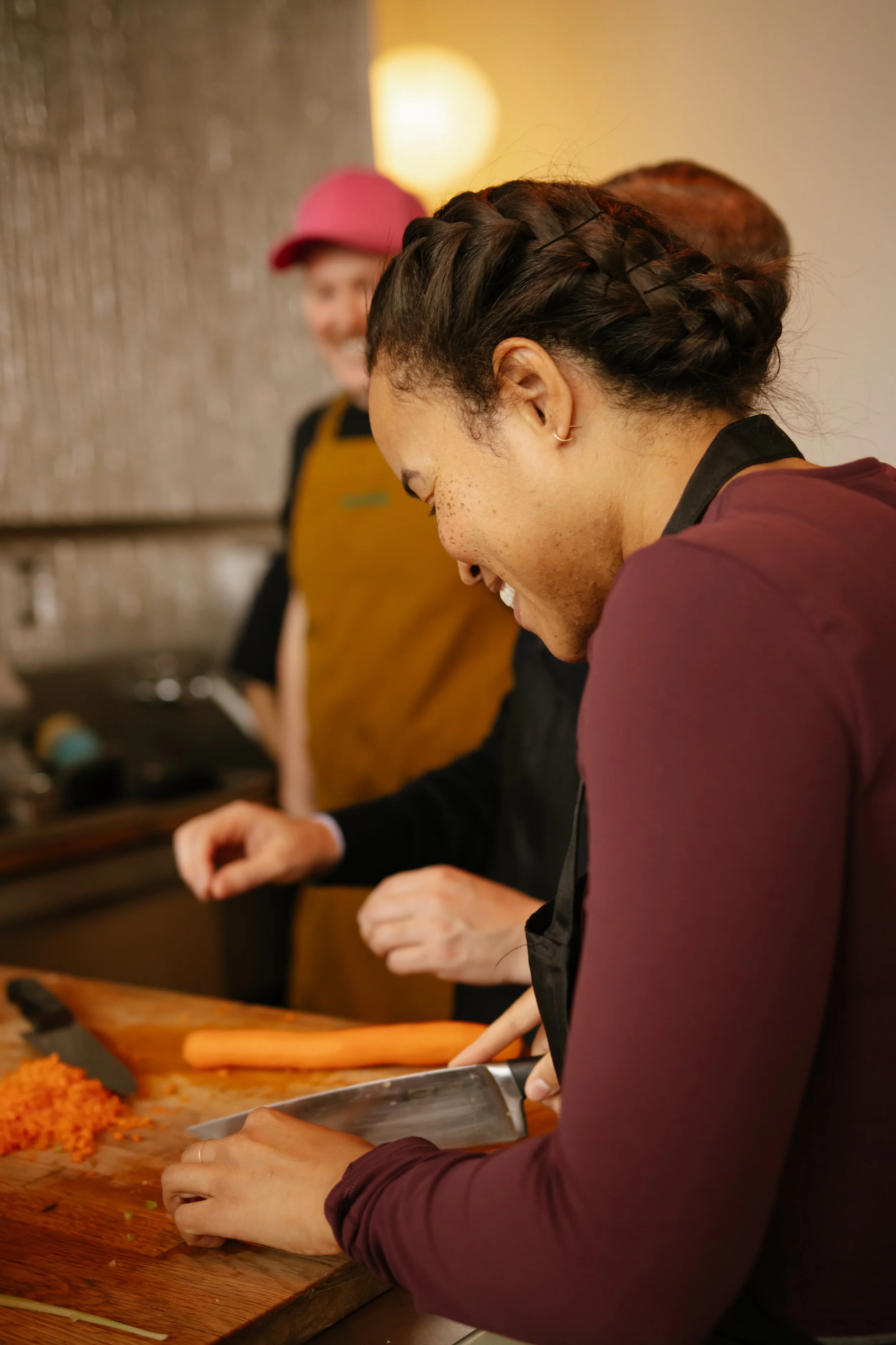 People chopping vegetables in a kitchen, with one person smiling and wearing an apron.
