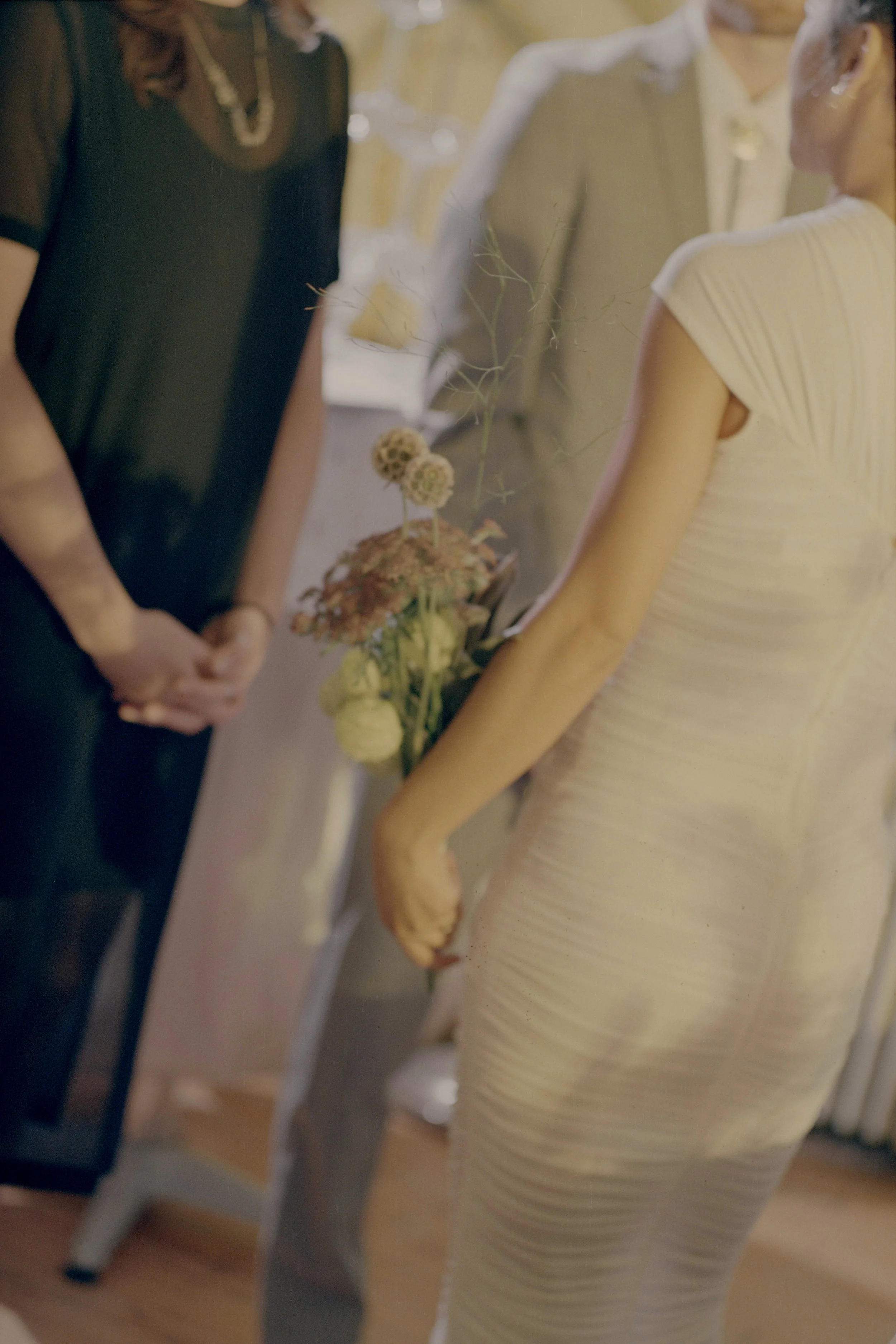 People in formal attire exchanging vows, with one holding a bouquet of flowers, possibly at a wedding ceremony.