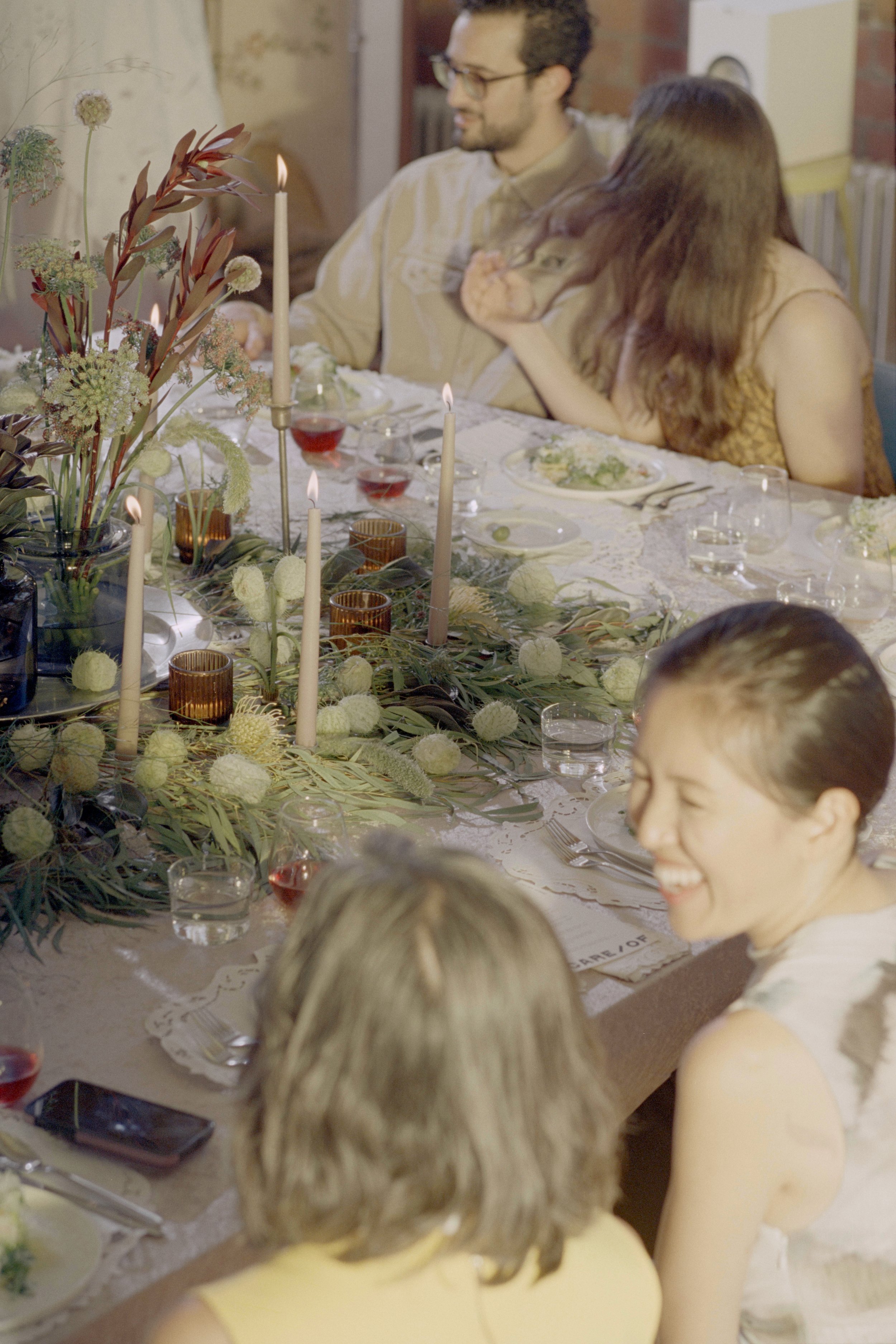 People sitting at a decorated dinner table with flowers and candles, having a meal and socializing.