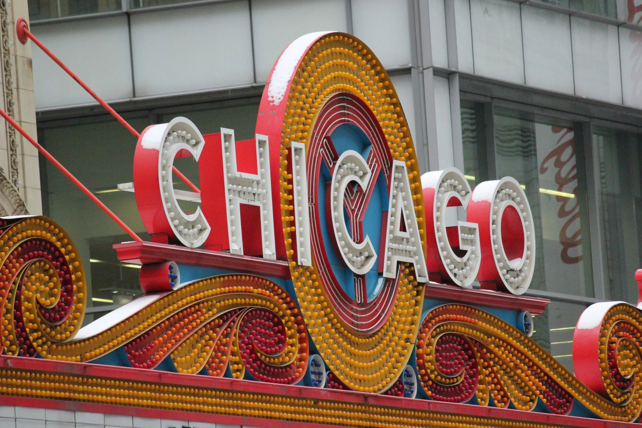 Photograph of the neon sign that reads “Chicago.” The letters of the word are in white lights, with festoons of red and yellow lights below and a yellow circle of lights behind.