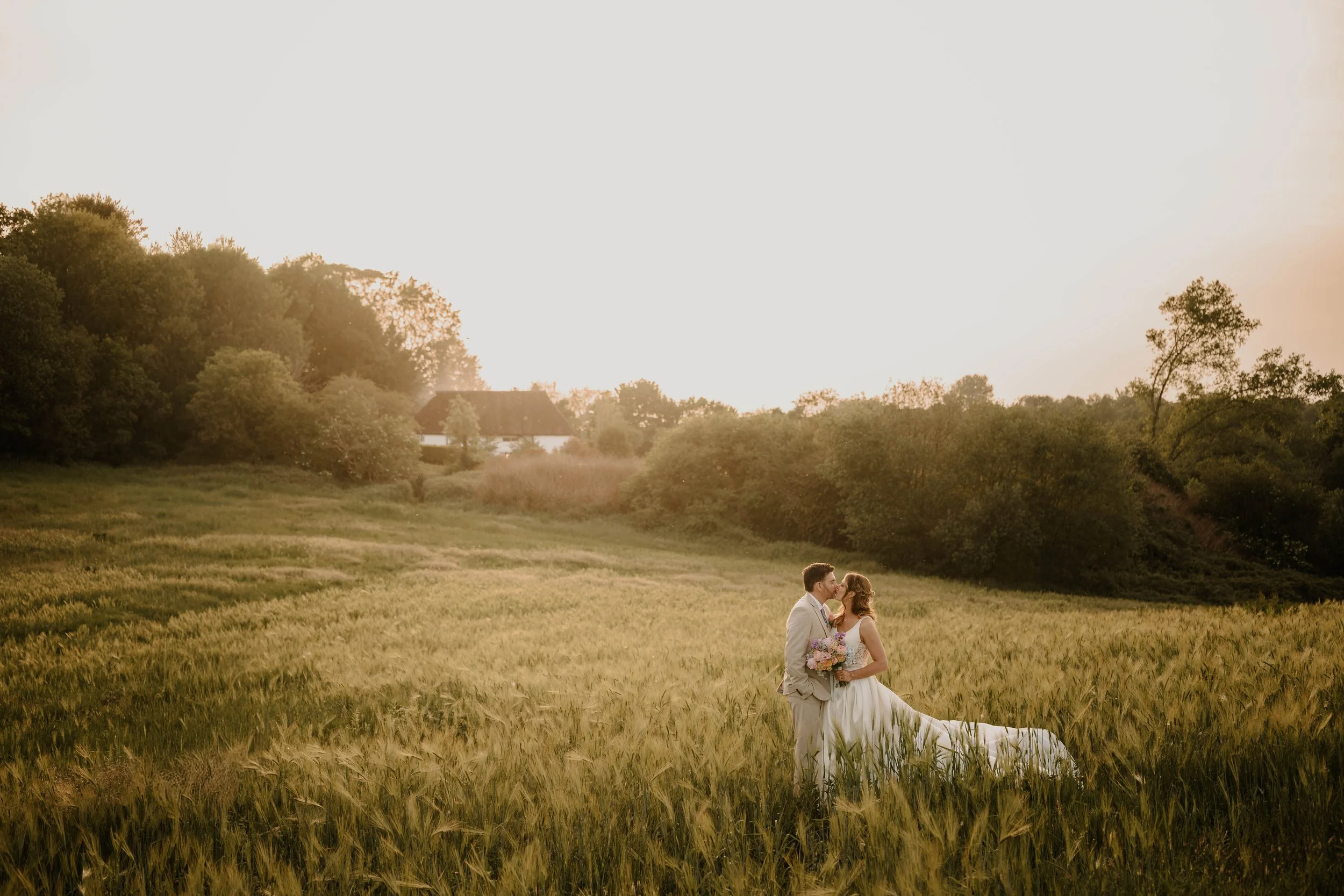 bride and groom kissing in a field at sunset with the Orchard Suite behind them