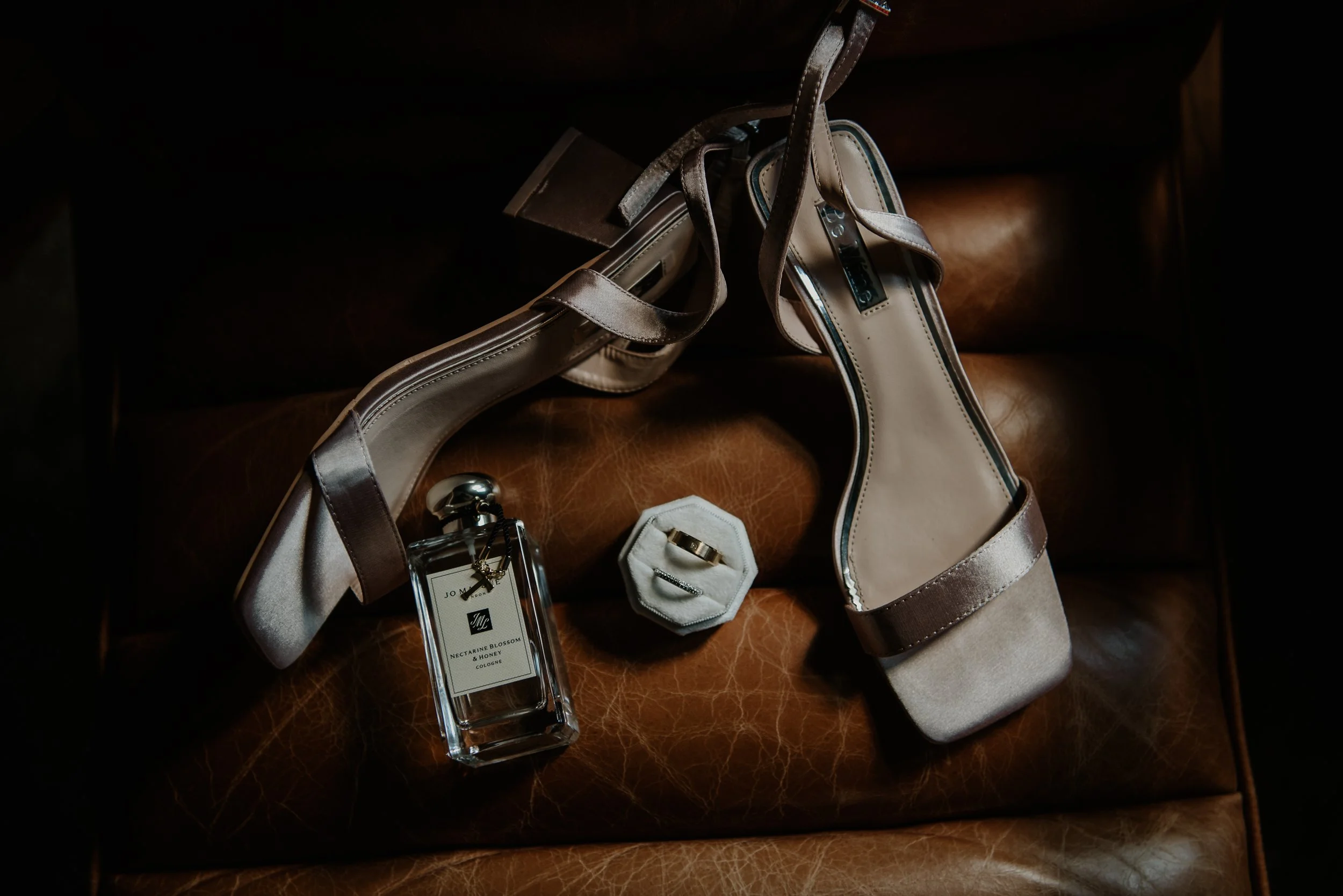 Wedding rings, perfume and shoes positioned on a leather chair