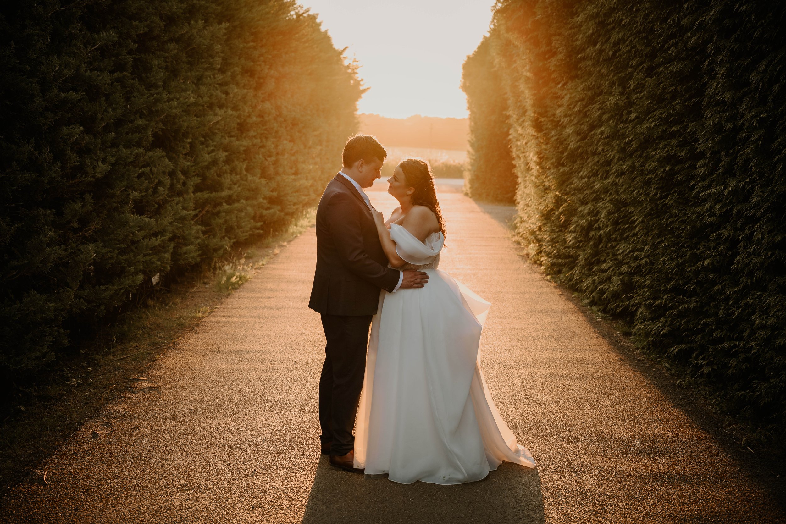 Bride and groom facing each other on the drive at Old Kent Barn as the sun sets behind them.
