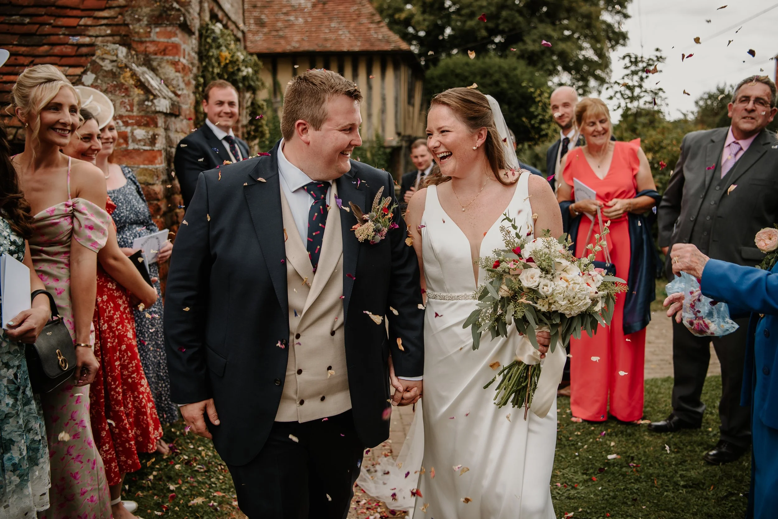Bride and groom smiling at each other as walking through confetti outside a church