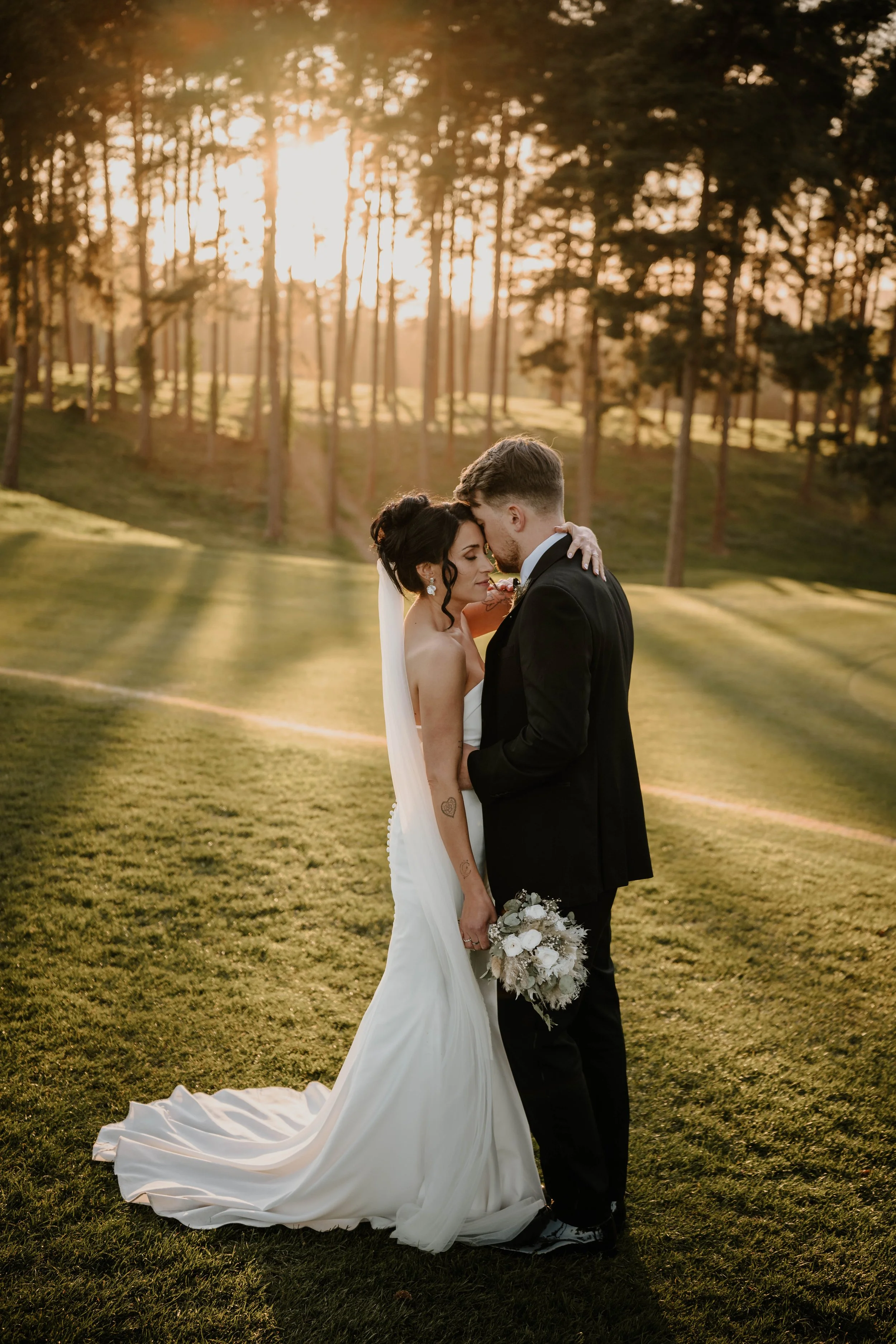 Bride and groom embracing together as the sun glows through the trees at Westerham Golf Club