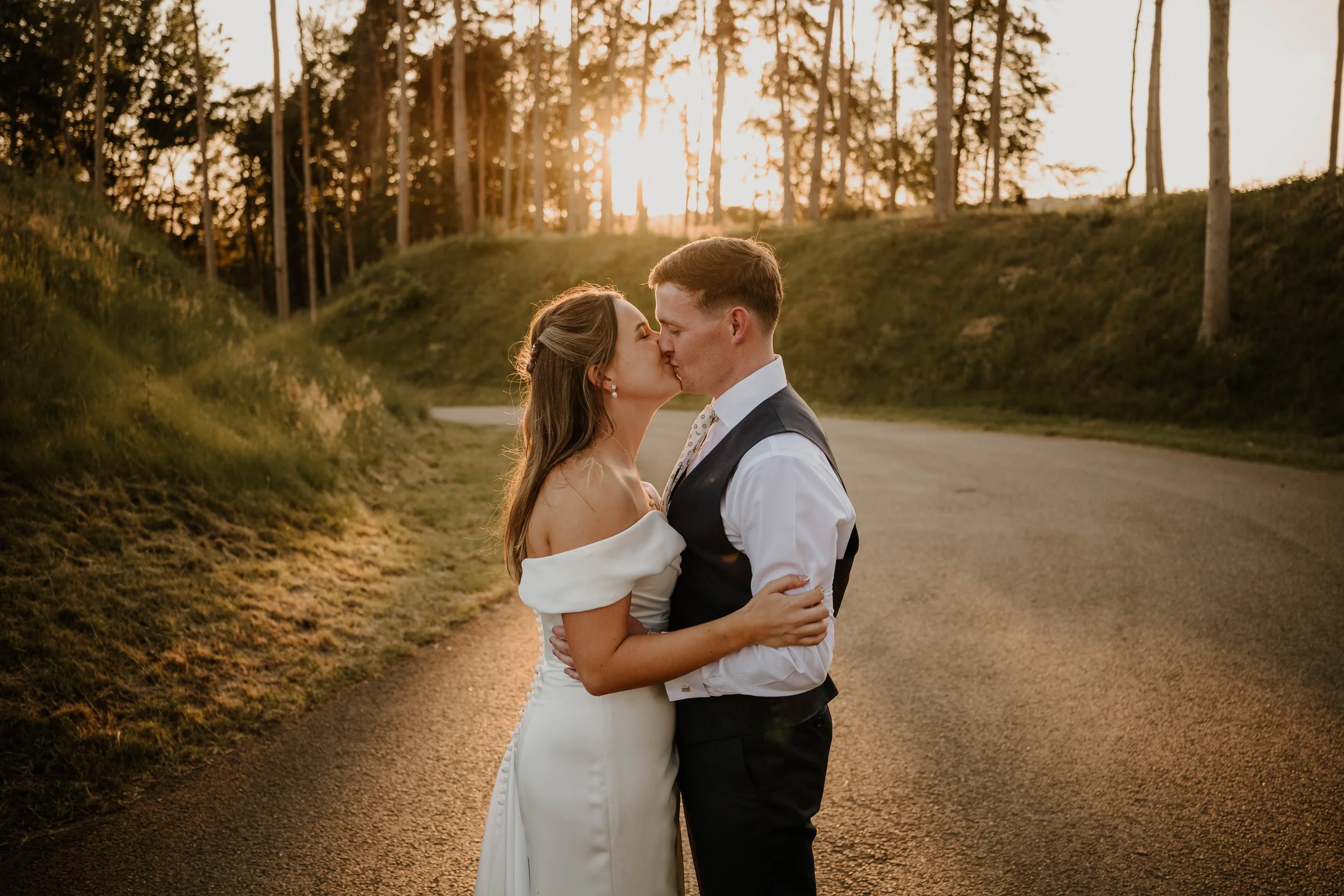 bride and groom kissing at the entrance of Westerham Golf Club, with the sun setting behind them.