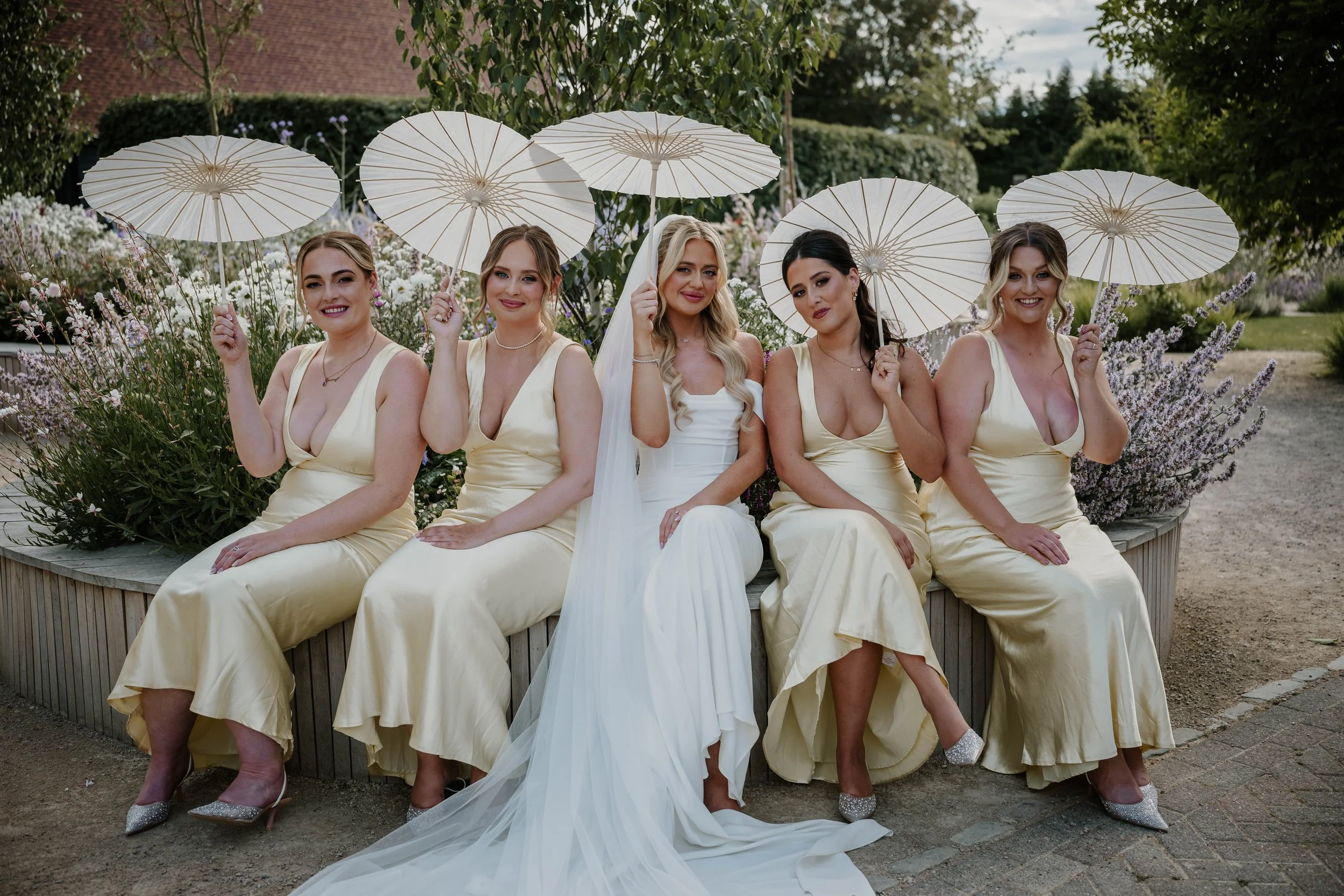 Bridesmaids sitting on bench with paper umbrellas at Old Kent Barn