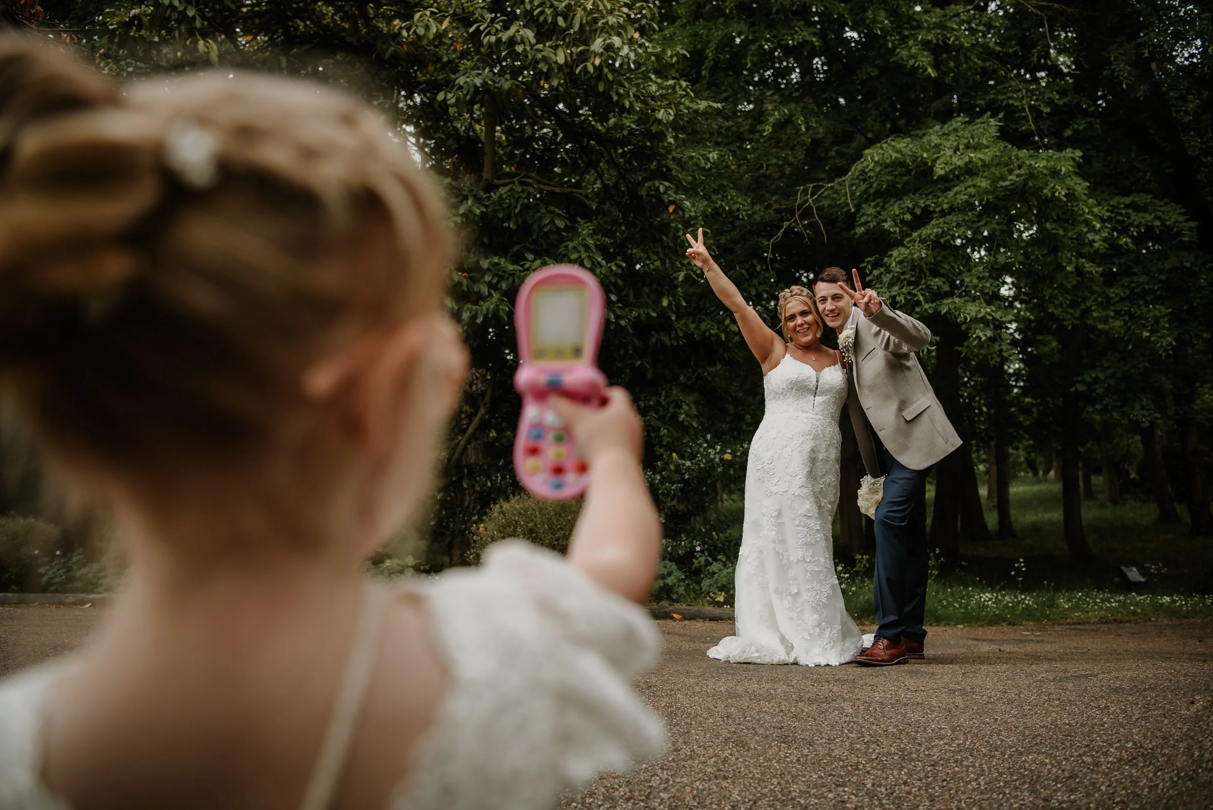 Bride and groom posing for their daughter to take a photo on a toy phone