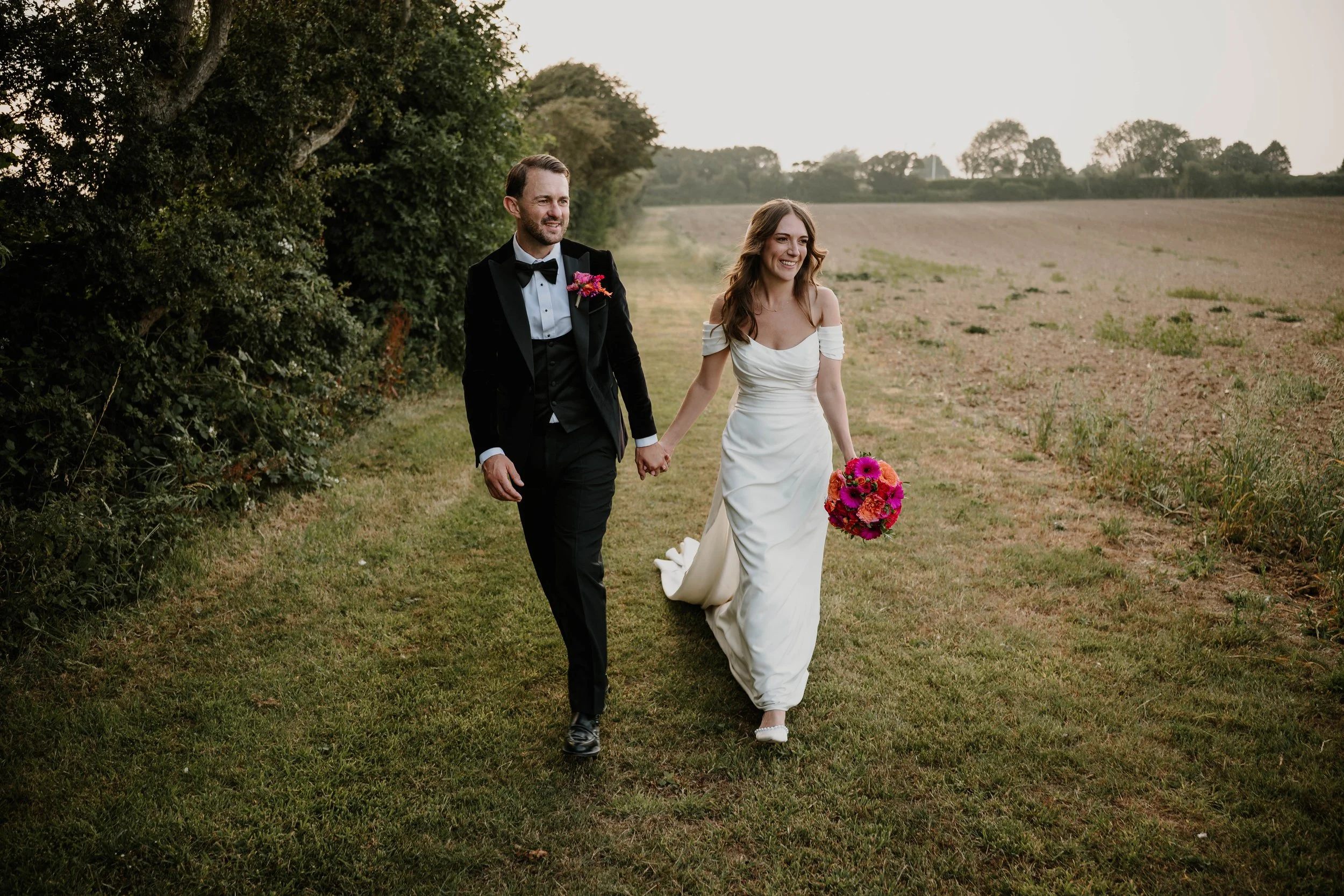 Bride and groom walking through a field, holding hands, at Reach Court Farm