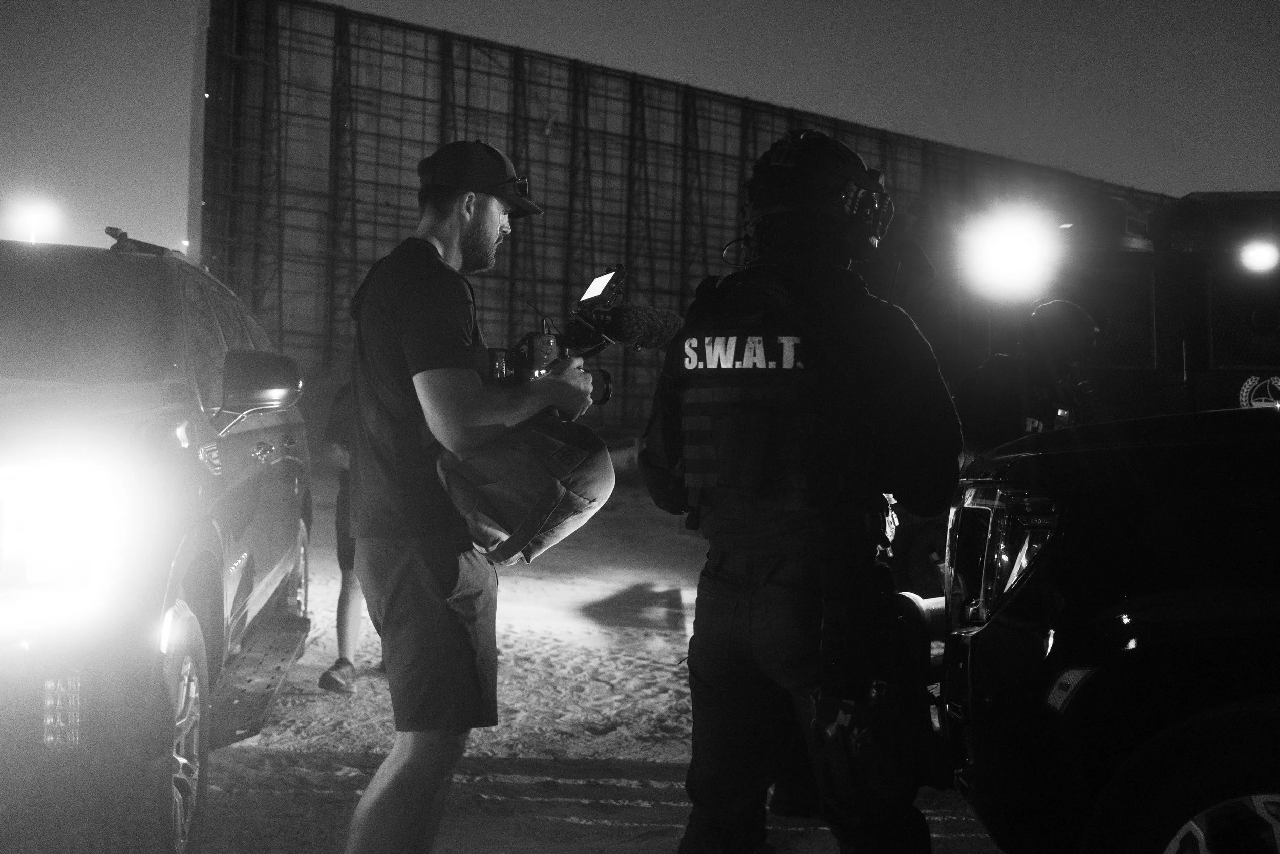 Tom Thessman - Nighttime scene showing a man with camera equipment and two SWAT officers near vehicles.