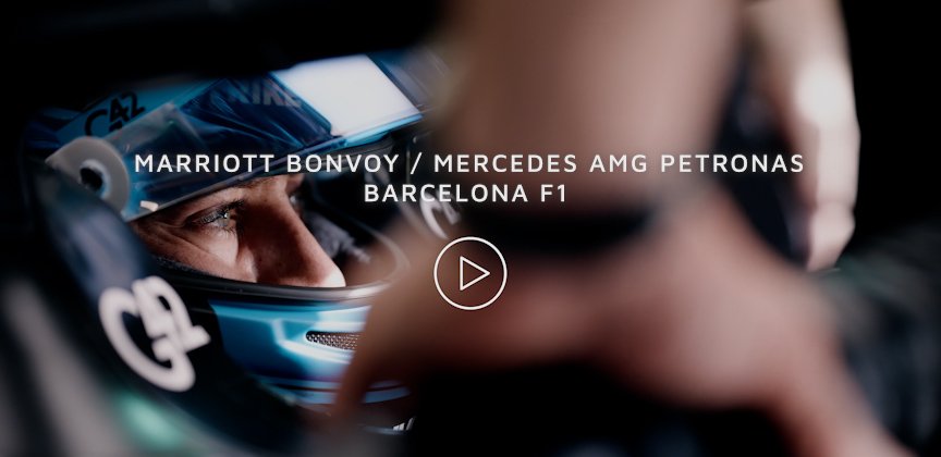 Close-up of race car driver wearing helmet and racing suit, with an overlay of text mentioning Mercedes AMG Petronas F1 team and Barcelona F1, and a play button in the center.