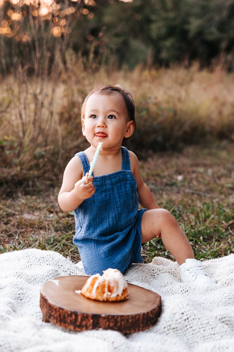Baby boy in blue suspenders eating 1st birthday cake