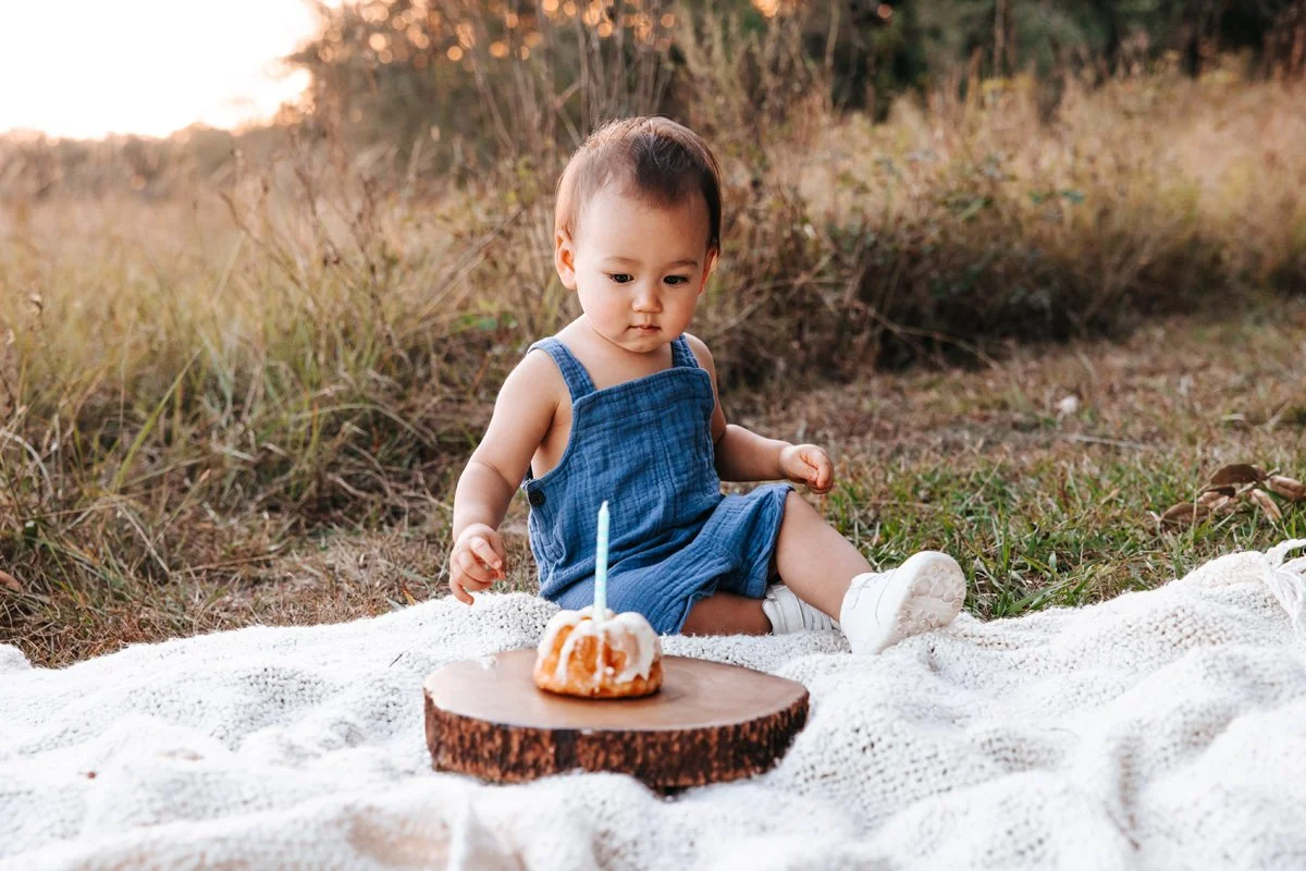 Baby boy in blue suspenders eating 1st birthday cake