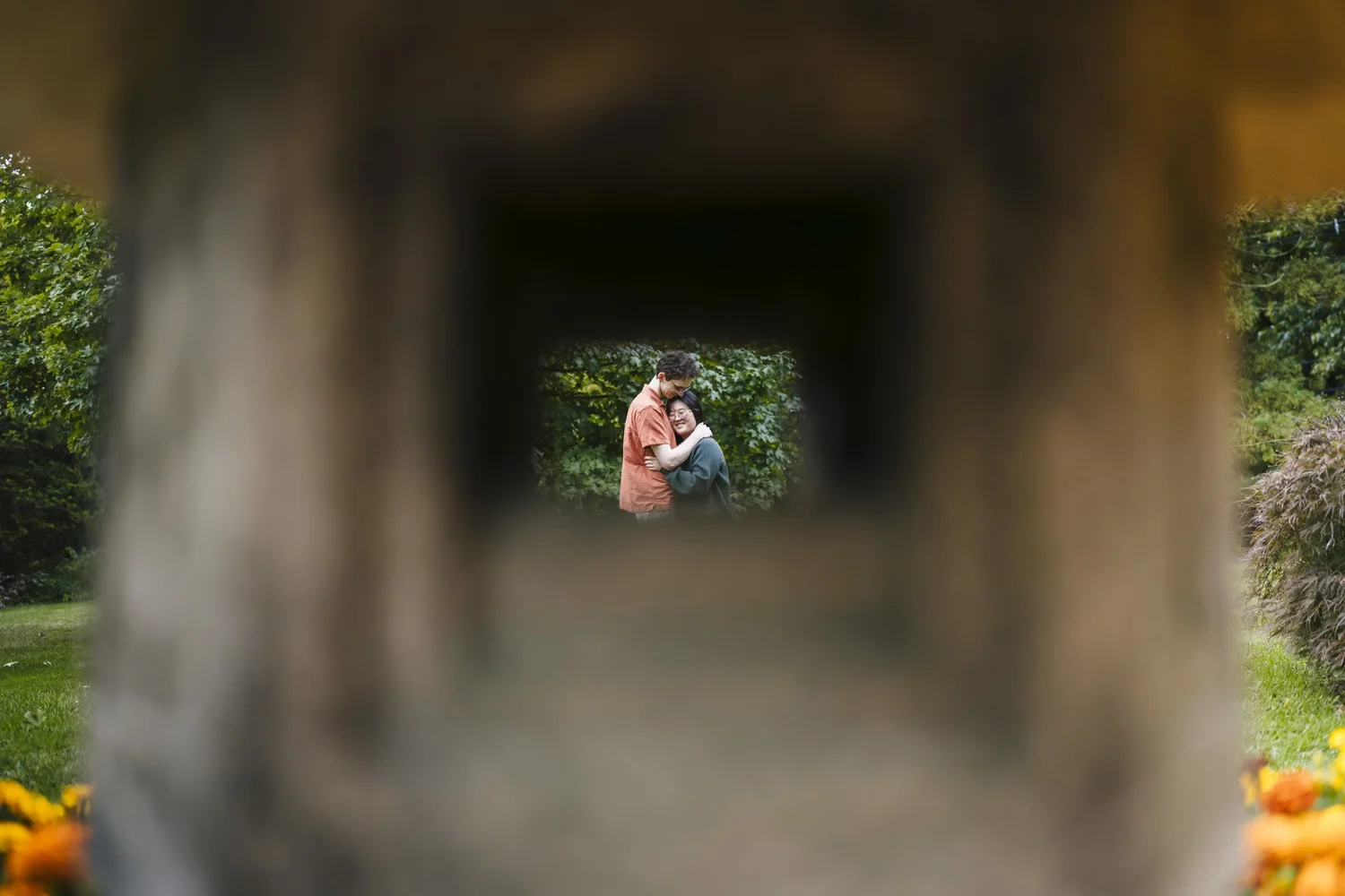 Couple embracing in a garden, framed through an opening in a wooden structure