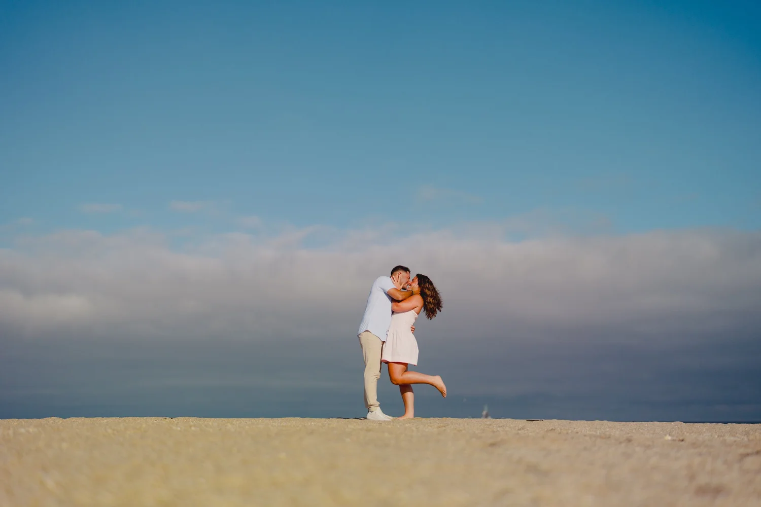 An engaged couple sharing a kiss beside the ocean.