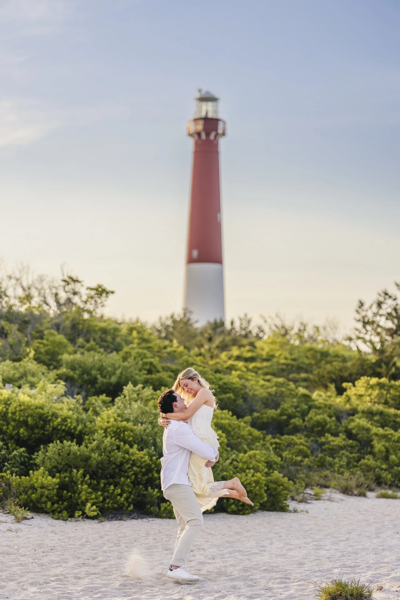 Couple sharing an embrace beneath a red and white lighthouse