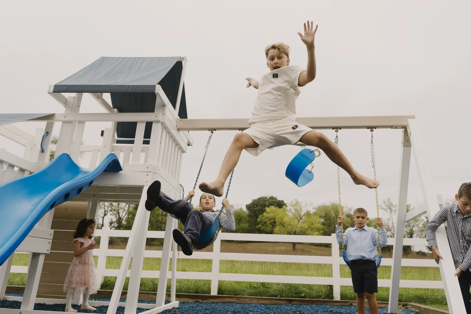 Children playing on the backyard swing set, with one boy airborne
