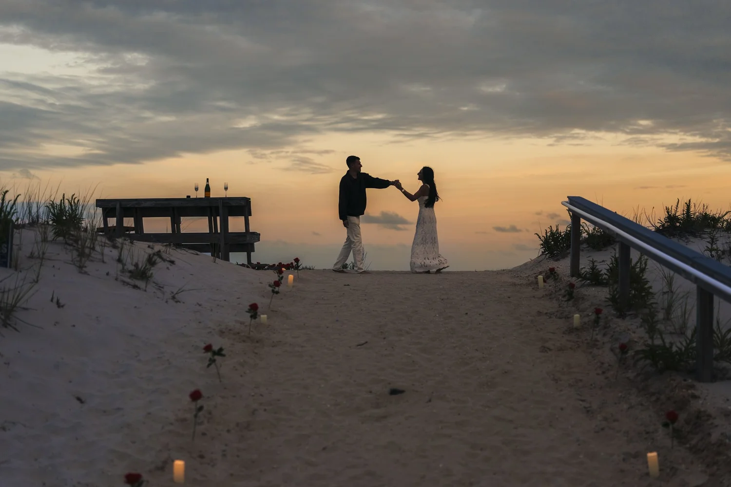 Silhouetted couple dancing beside a waterfront picnic table beneath a glowing sunset