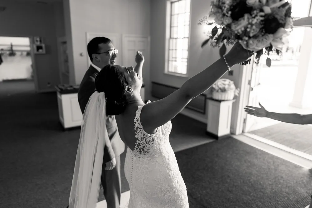 A bride raising her bouquet with her smiling groom behind her