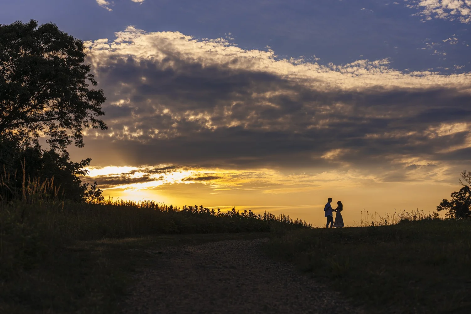 Distant couple silhouetted beneath dramatic clouds and golden sunset light