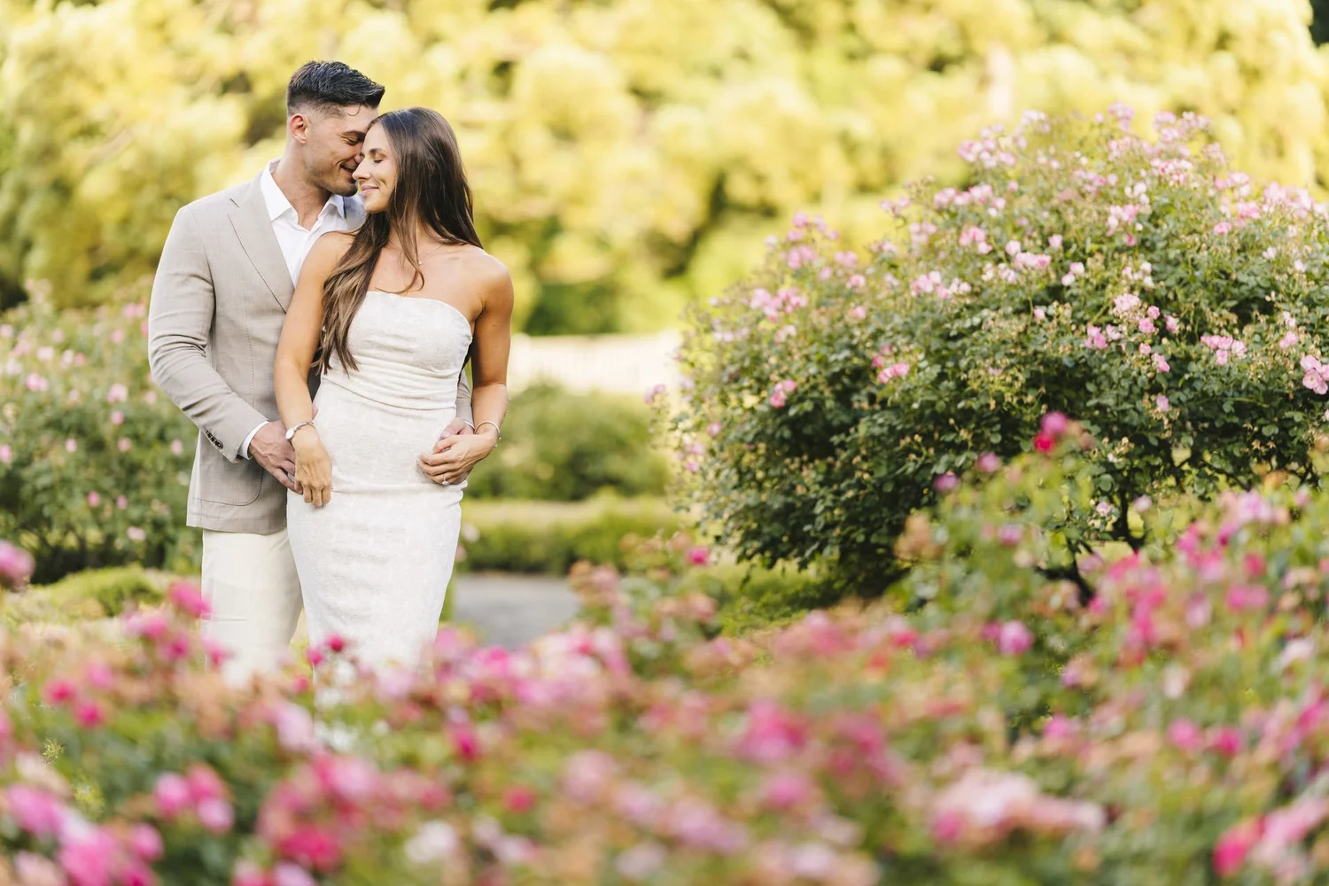 Couple embracing beside pink flowers in a sunlit garden