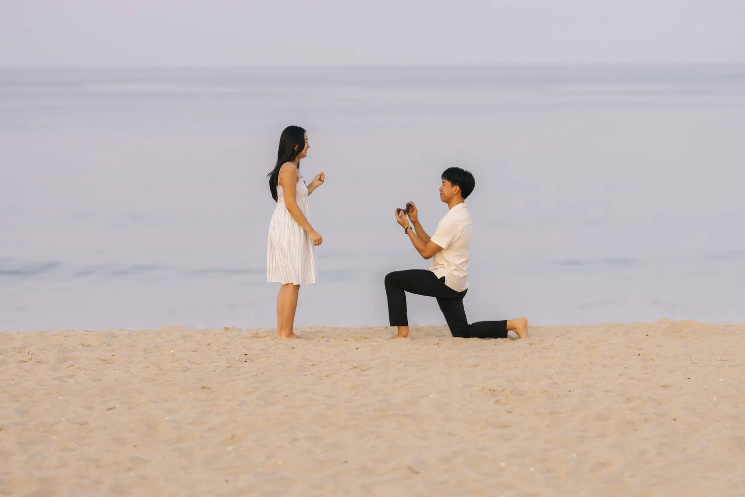 Barefoot man proposing on one knee to his partner on a quiet beach