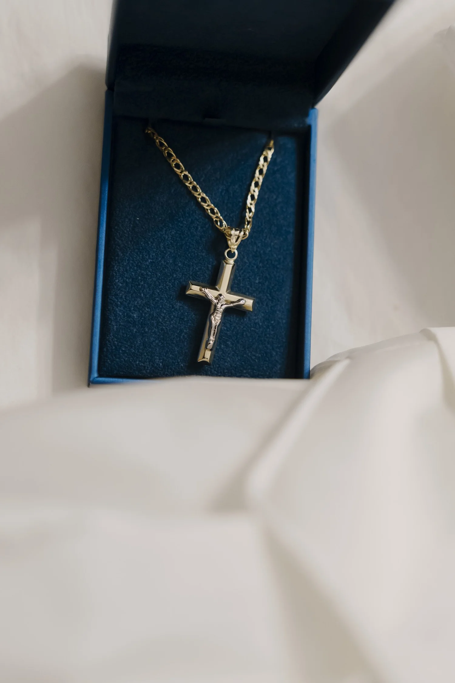 Gold cross necklace in a blue box beside white baptism clothing