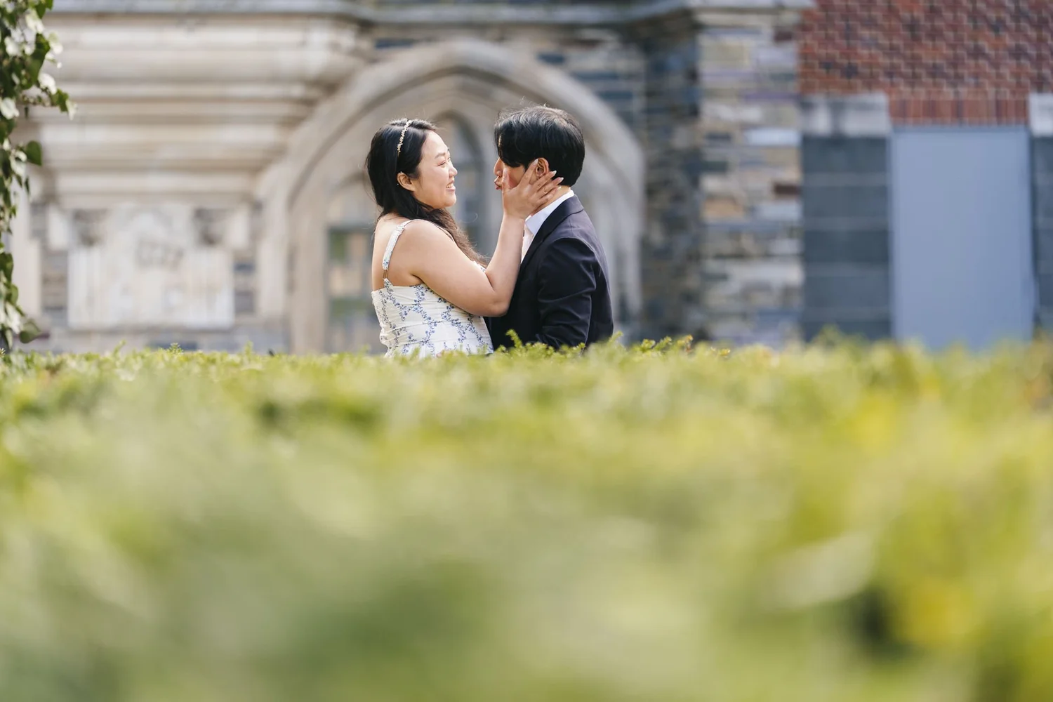 Couple sharing a close moment in front of an ornate stone building and green hedge