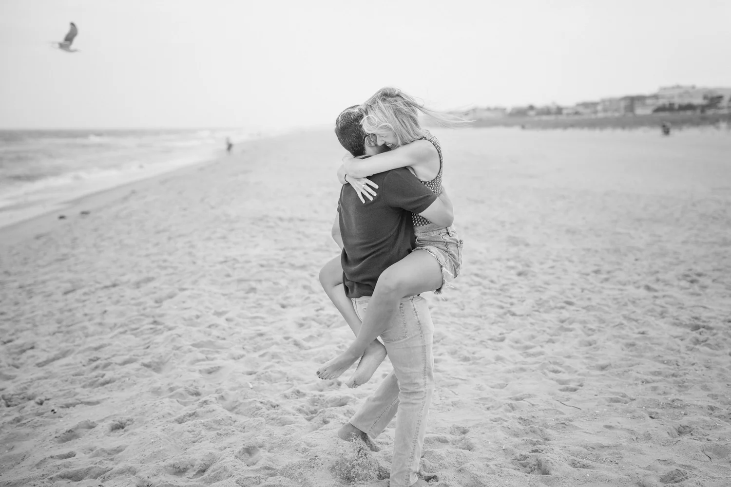 Black-and-white portrait of a couple embracing on the beach.