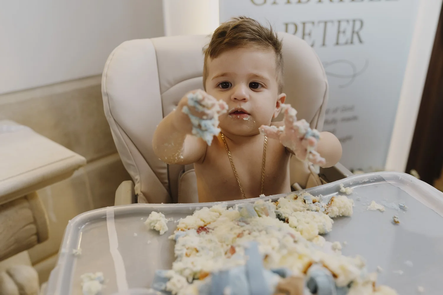 Gabriele enjoying cake in his high chair during his first birthday cake smash