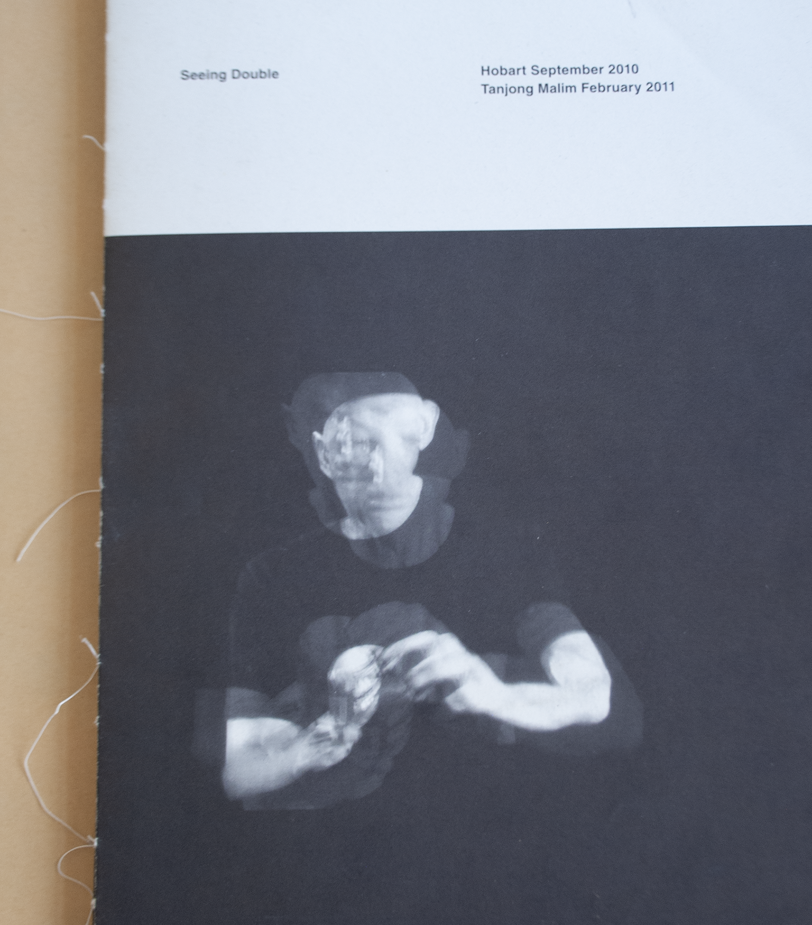 Black and white catalogue. The 1/3 portion on the top is white with the title Seeing Double. 3/4 of the page below it is a man on a black background and his image is in double form or like a motion picture.