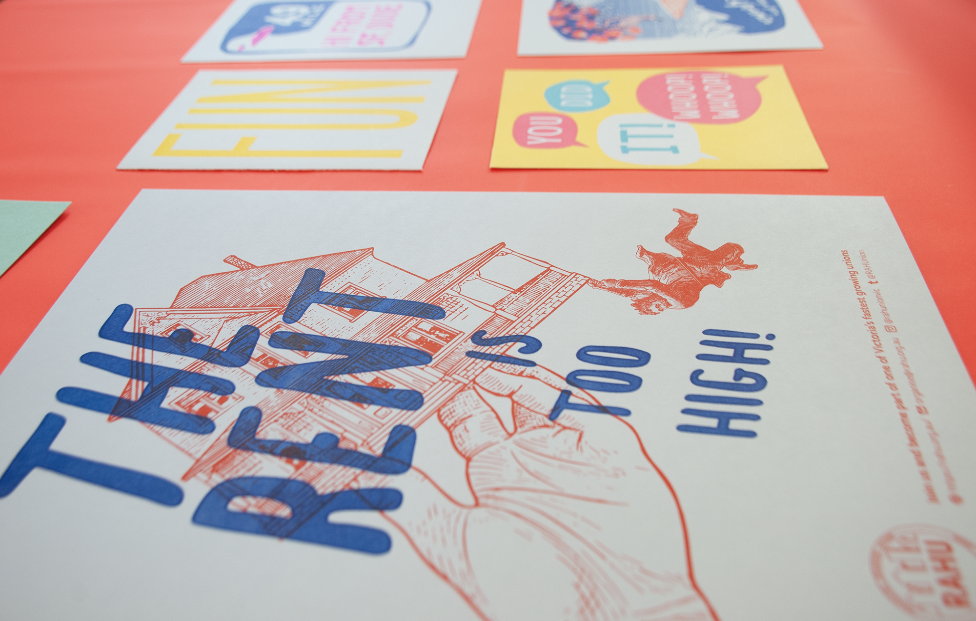 A close-up of the poster lying on a red-colored desk. Beside it are more posters with different texts and styles
