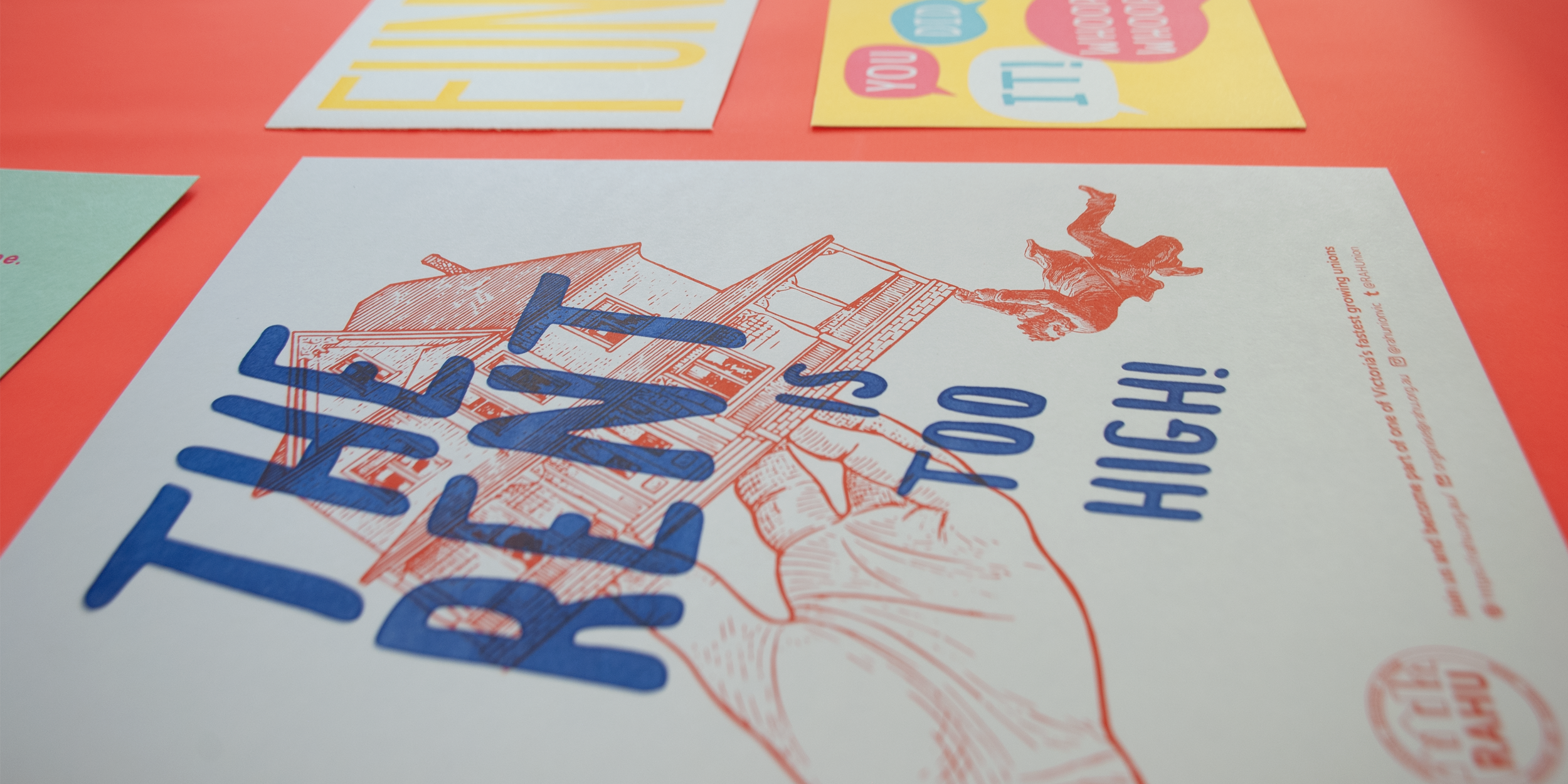 A close-up of the poster lying on a red-colored desk. Beside it are more posters with different texts and styles