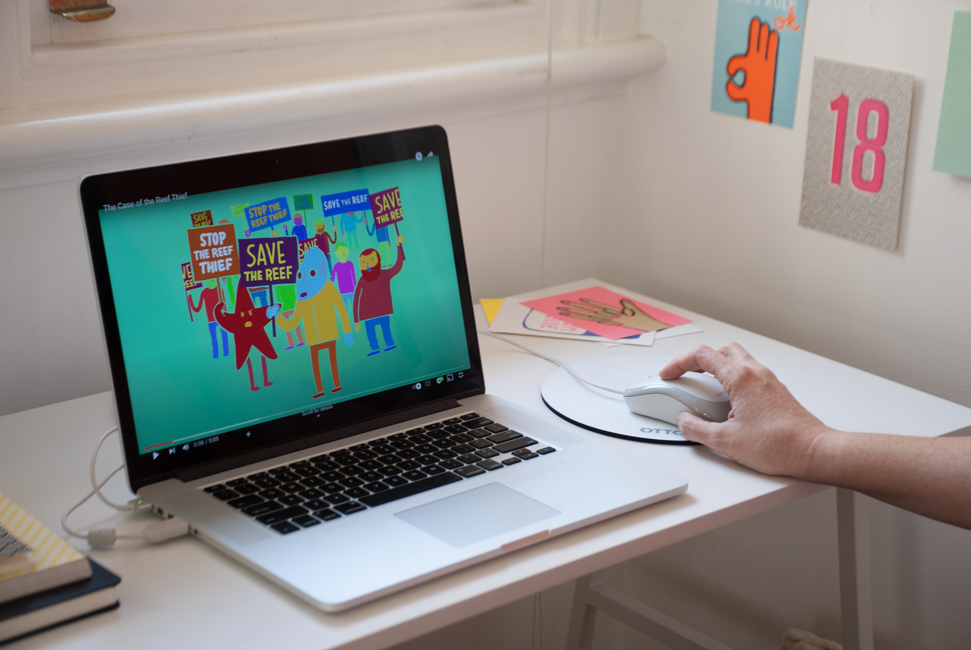 A laptop screen that shows an illustration of a fish holding a sign that says Save the Reef with humans and other maritime characters behind it.