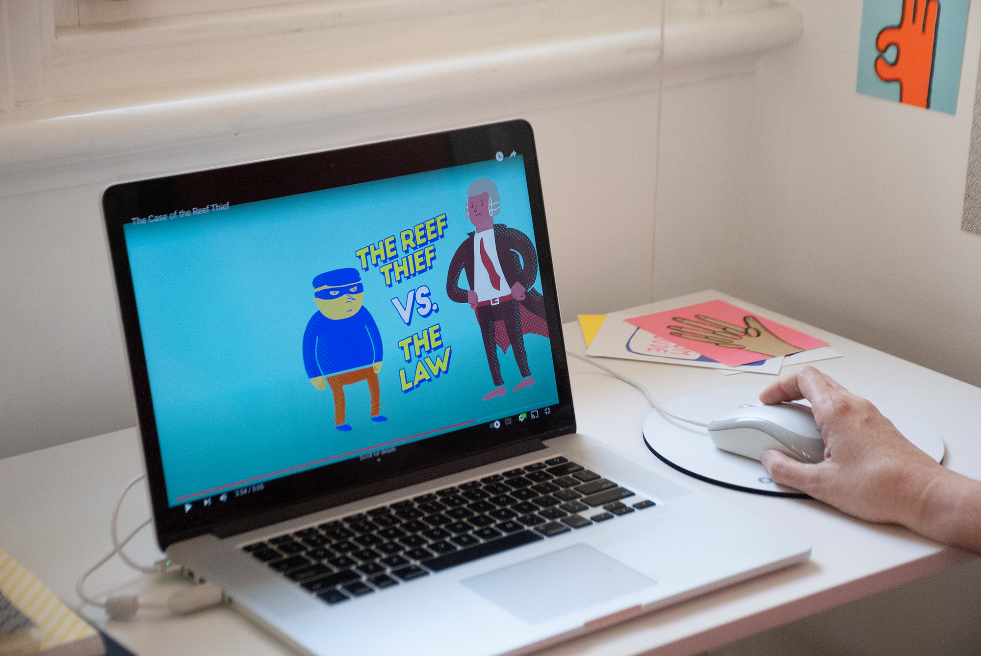 A laptop screen showing an illustration of man in mask dressed like a thief and a man on the right with a cape. The texts between them reads The Reef Thief versus the Law