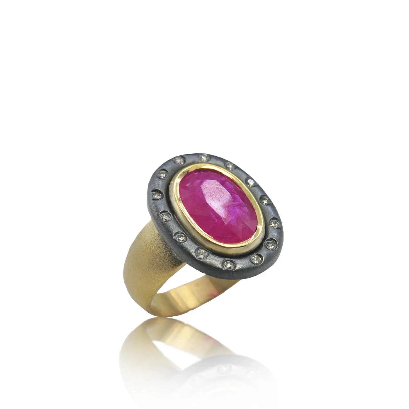 Bright pink faceted ruby ring with a diamond halo and mixed metal setting. Thick 18k gold band and oxidized black silver.