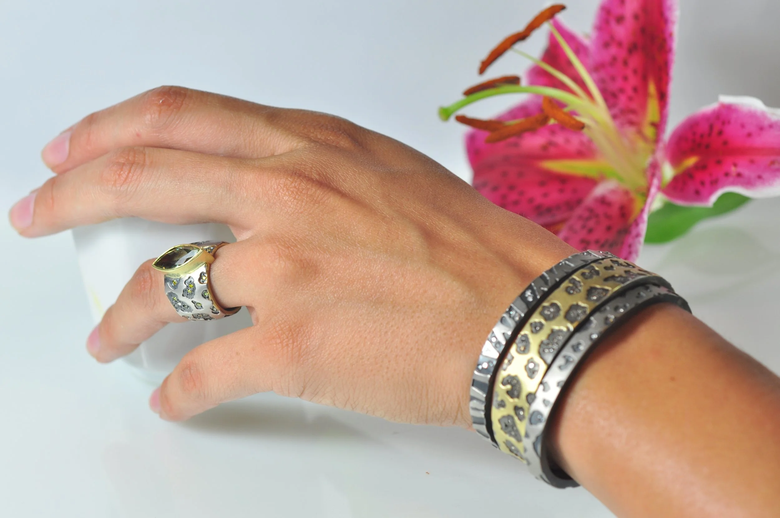 Stacked animal print bracelets on white woman with pink flower. Handcrafted fine art jewelry by Rebecca Myers Design.