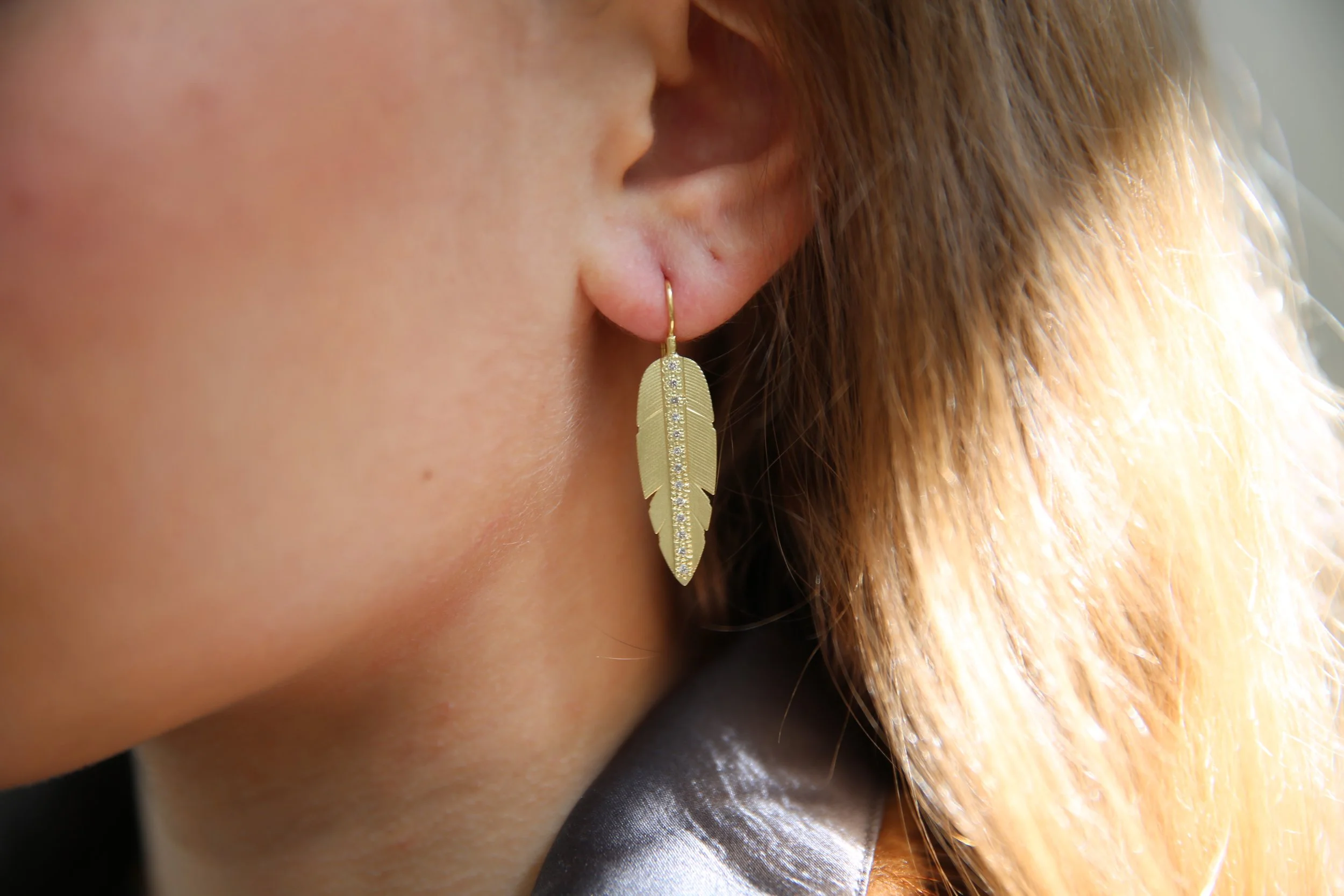 Large feather earrings in 18k yellow gold with channel set white diamonds on white woman model. Handmade fine art jewelry by Rebecca Myers Design.