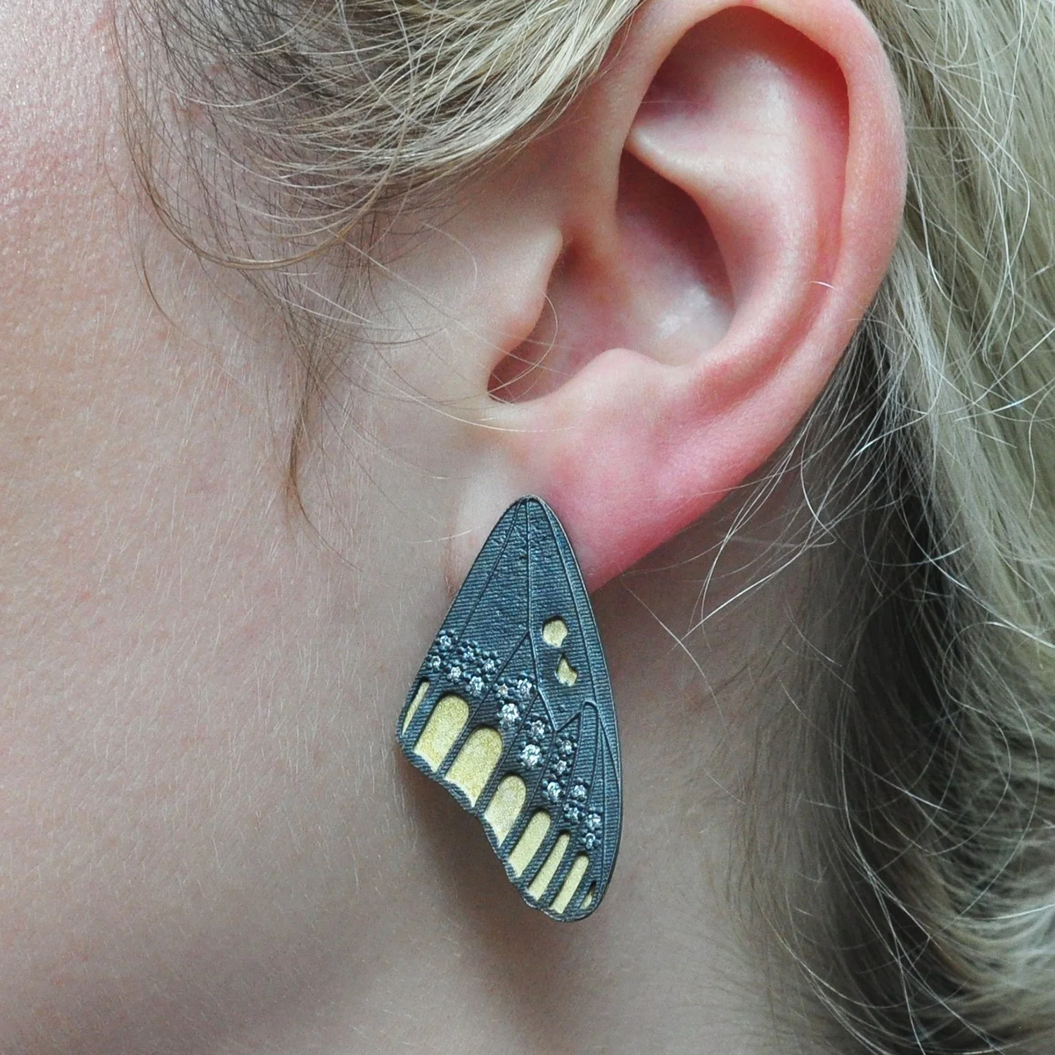Checkerspot Top Wing Earrings. 18k yellow gold, oxidized silver, diamonds. Shown on white female model. Handmade fine art jewelry by Rebecca Myers Design.