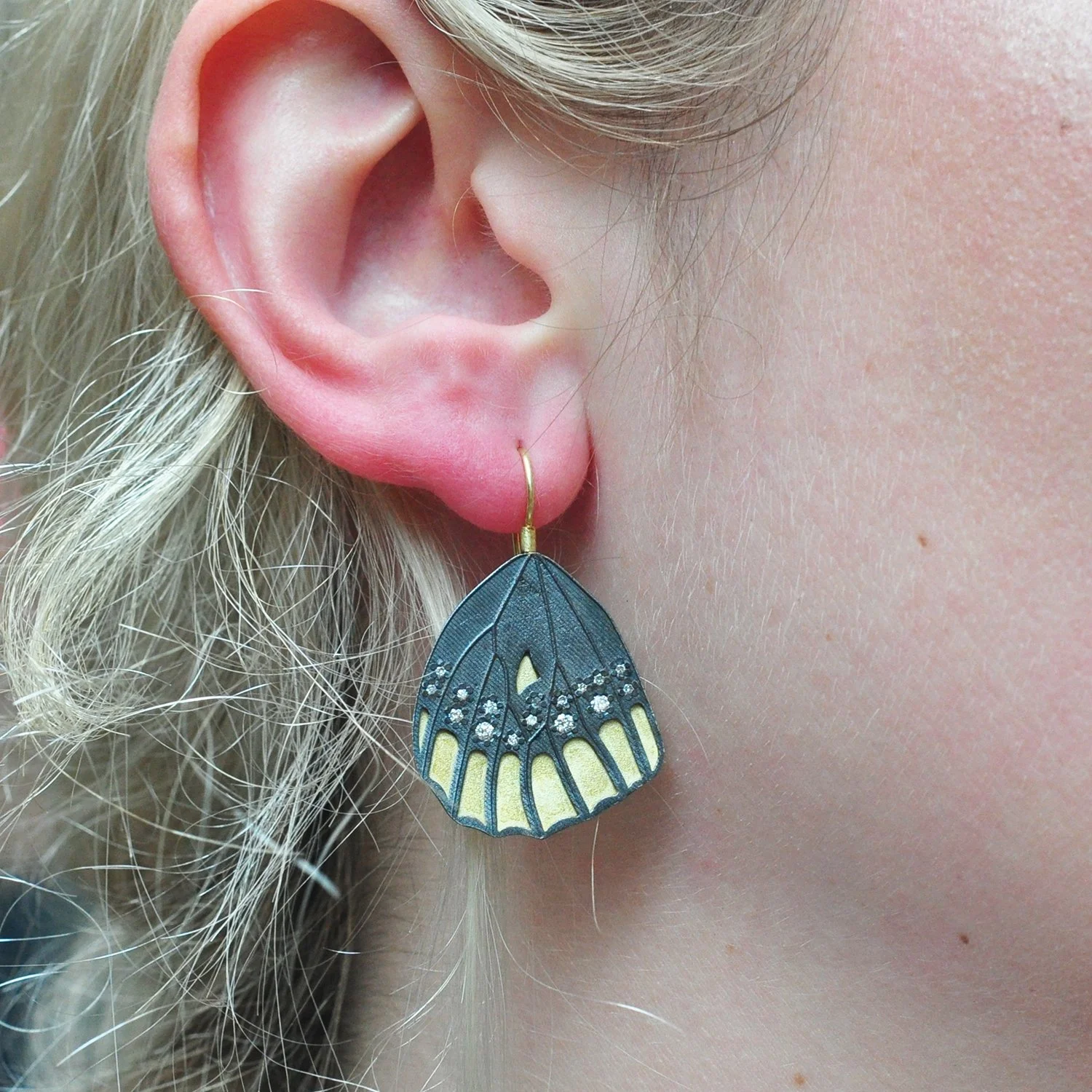 Checkerspot Bottom Wing Earrings. 18k yellow gold, oxidized silver, diamonds. Shown on white female model. Handmade fine art jewelry by Rebecca Myers Design.