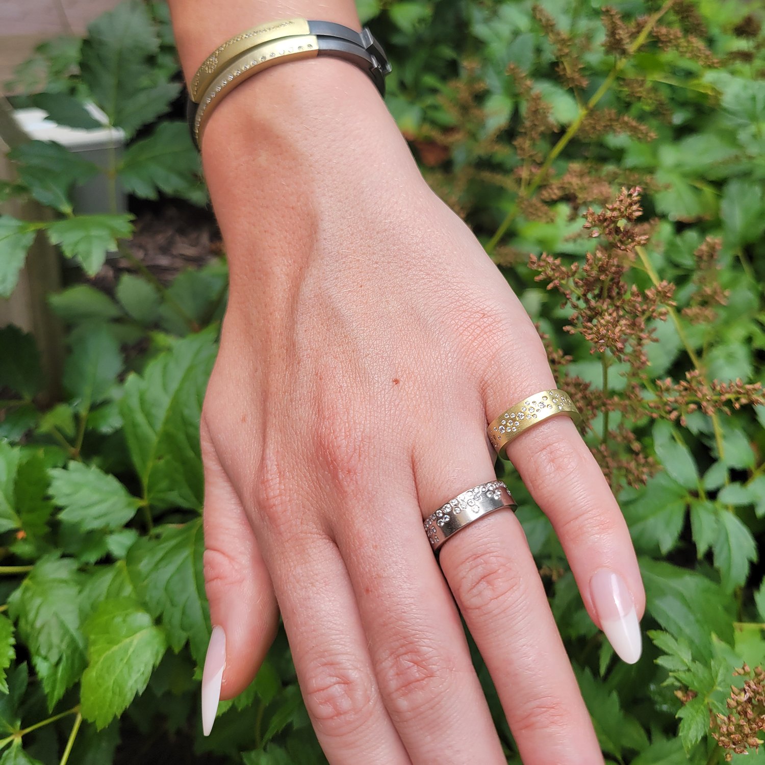 Round Fairy Dust Rings. 18k yellow gold, palladium, flush set white diamonds. Shown here on white female model. Handmade fine art jewelry by Rebecca Myers Design.