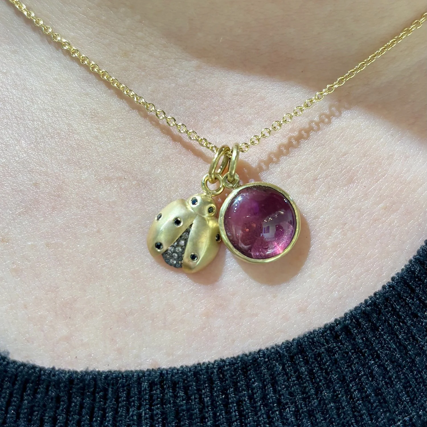 Ladybug & Pink Tourm Charms. 14k yellow gold, oxidized silver, white diamonds, marquis tourmaline cabochon. On white female model. Handmade fine art jewelry by Rebecca Myers Design.