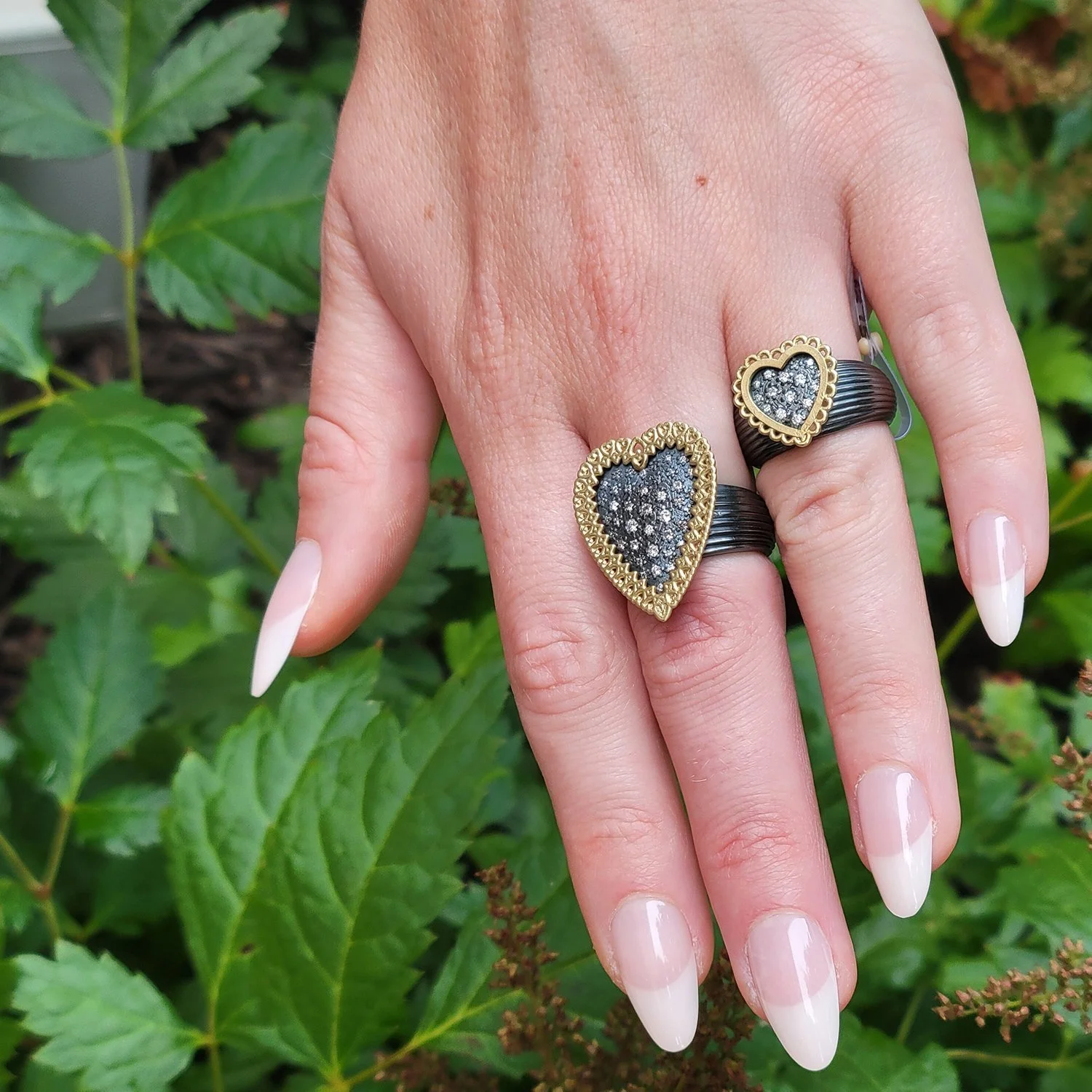 Framed Heart Rings. 14k yellow gold, oxidized silver, pave set white diamonds. On white female model. Handmade fine art jewelry by Rebecca Myers Design.