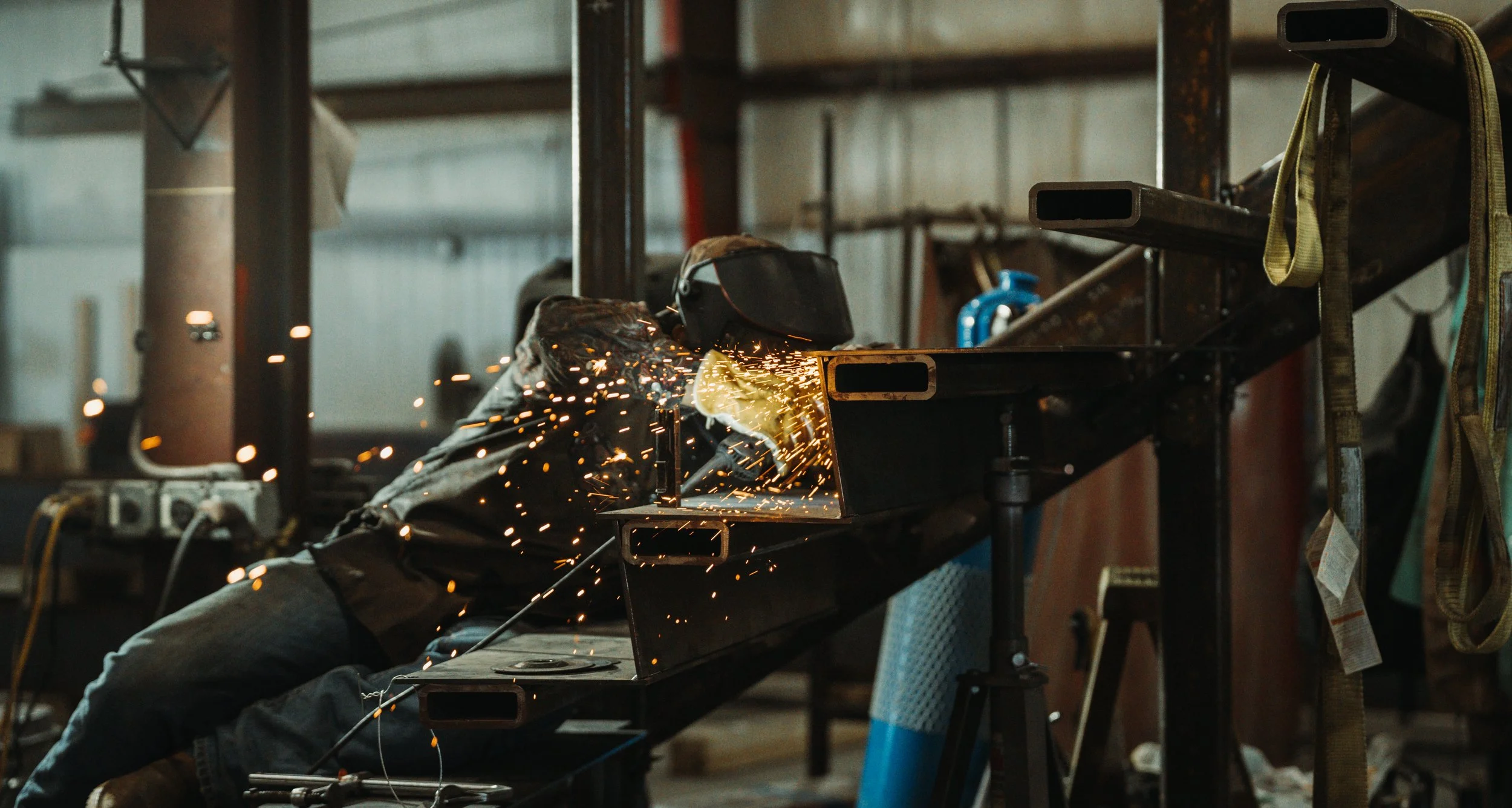 A person welding metal on a workbench in a workshop, with sparks flying from the welding process.