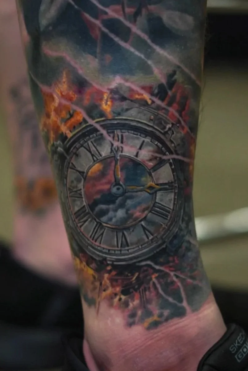 Tattoo of a clock with Roman numerals on a person’s arm, showing a sky scene with clouds and colors of a sunset or sunrise.