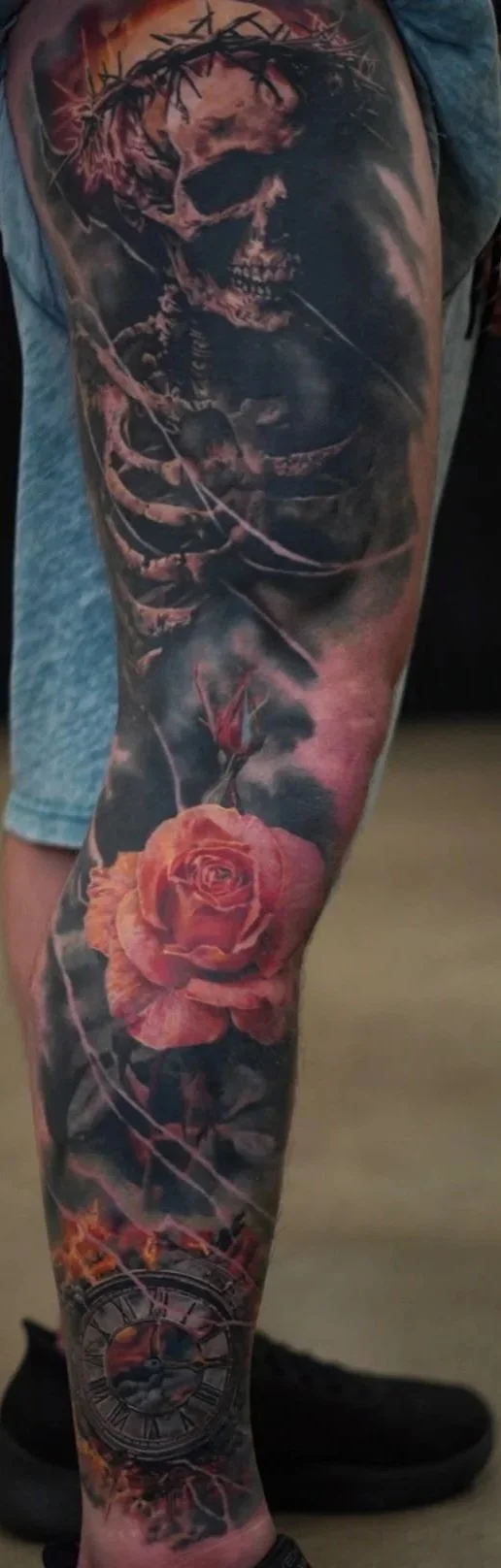 Colorful tattoo of a skull with a crown of thorns at the top, a flower near the knee, and a clock at the bottom of the leg.