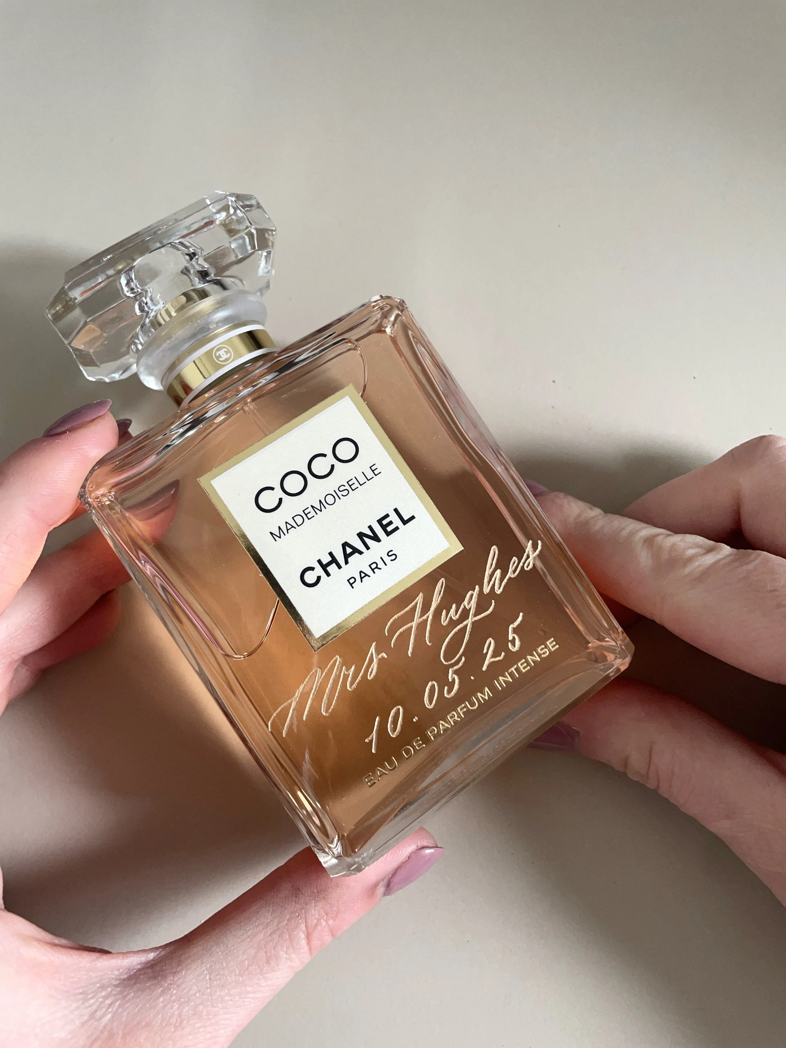 A person holding a Chanel Coco Mademoiselle perfume bottle with a pink liquid and a clear, faceted glass cap.