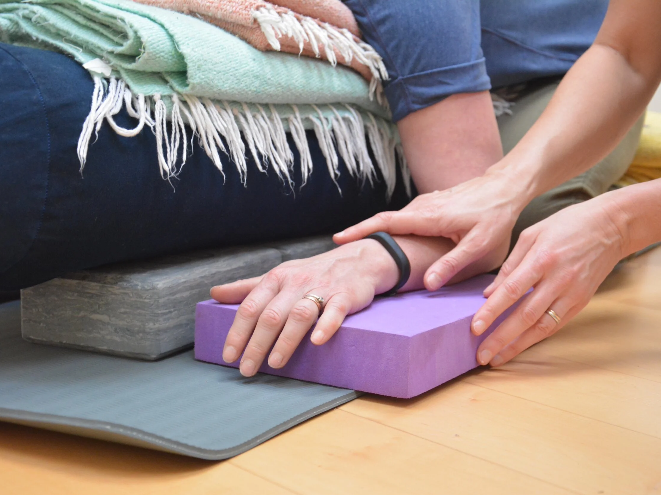 A person using a purple yoga block to perform a stretch or exercise while another person supports their arm.