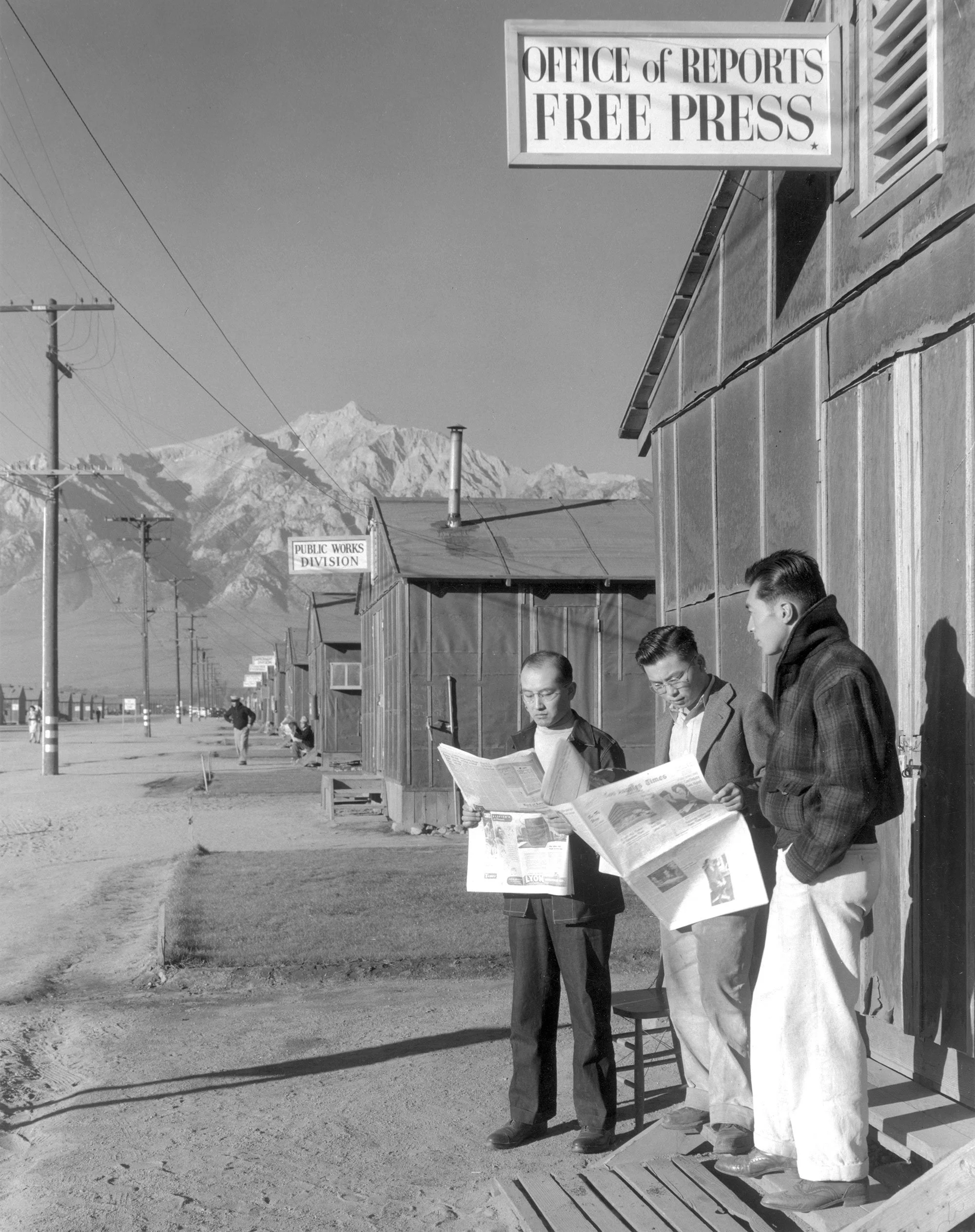 Roy Takeno, editor, and group reading paper in front of office, Manzanar Relocation Center, California